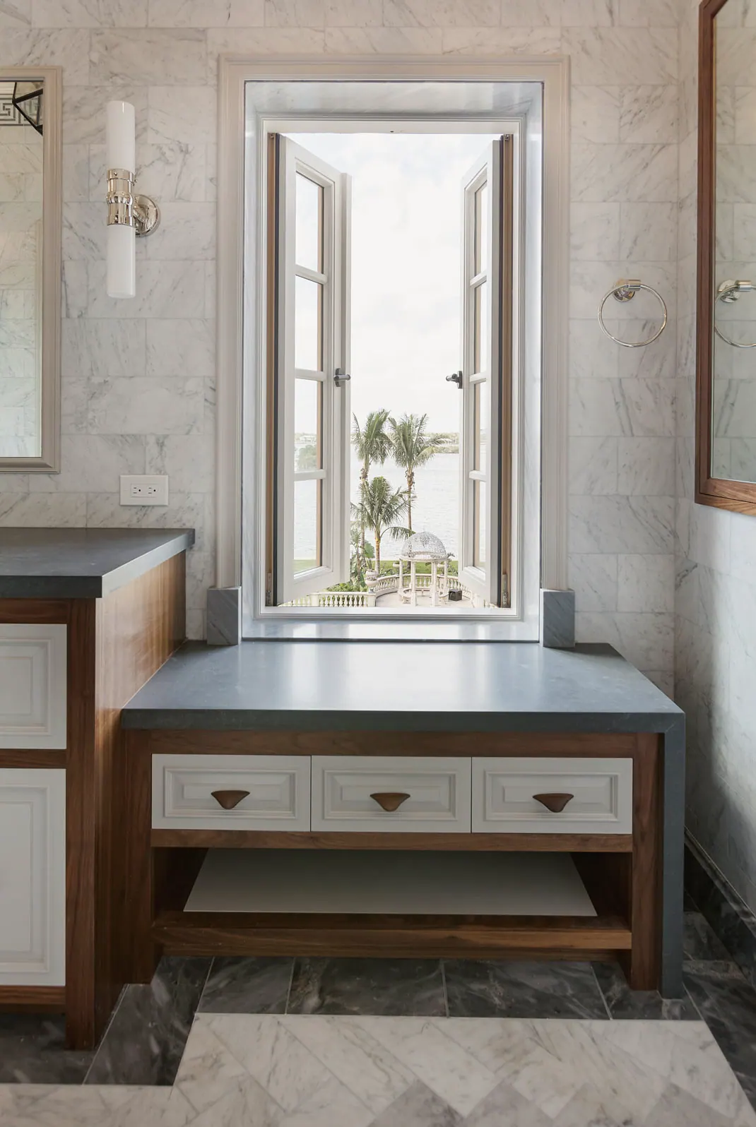 Wood vanity under a window in a marble bath