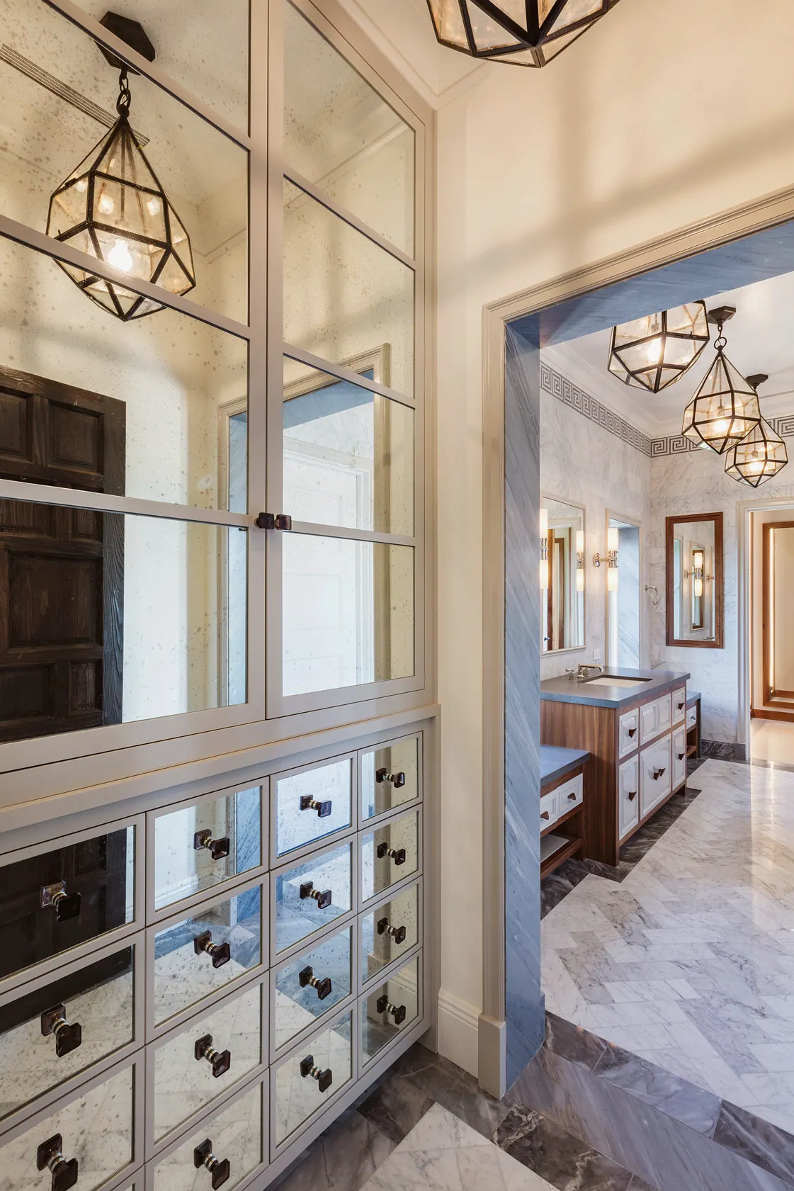 Mirrored cabinet wall in a dressing passage that opens to a marble bath