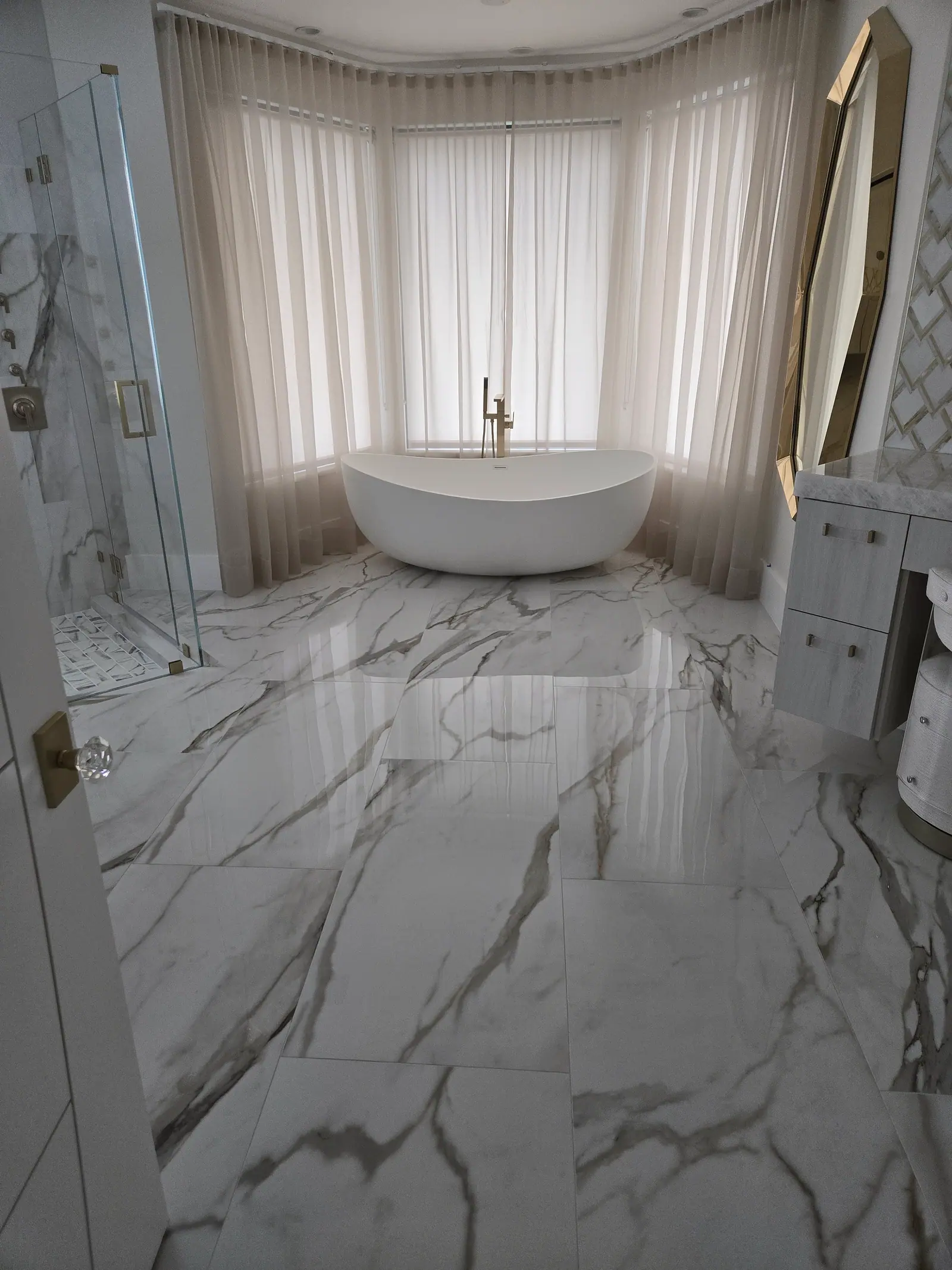 Freestanding tub in a curtained bay window with gold floor filler and polished large-format marble floor