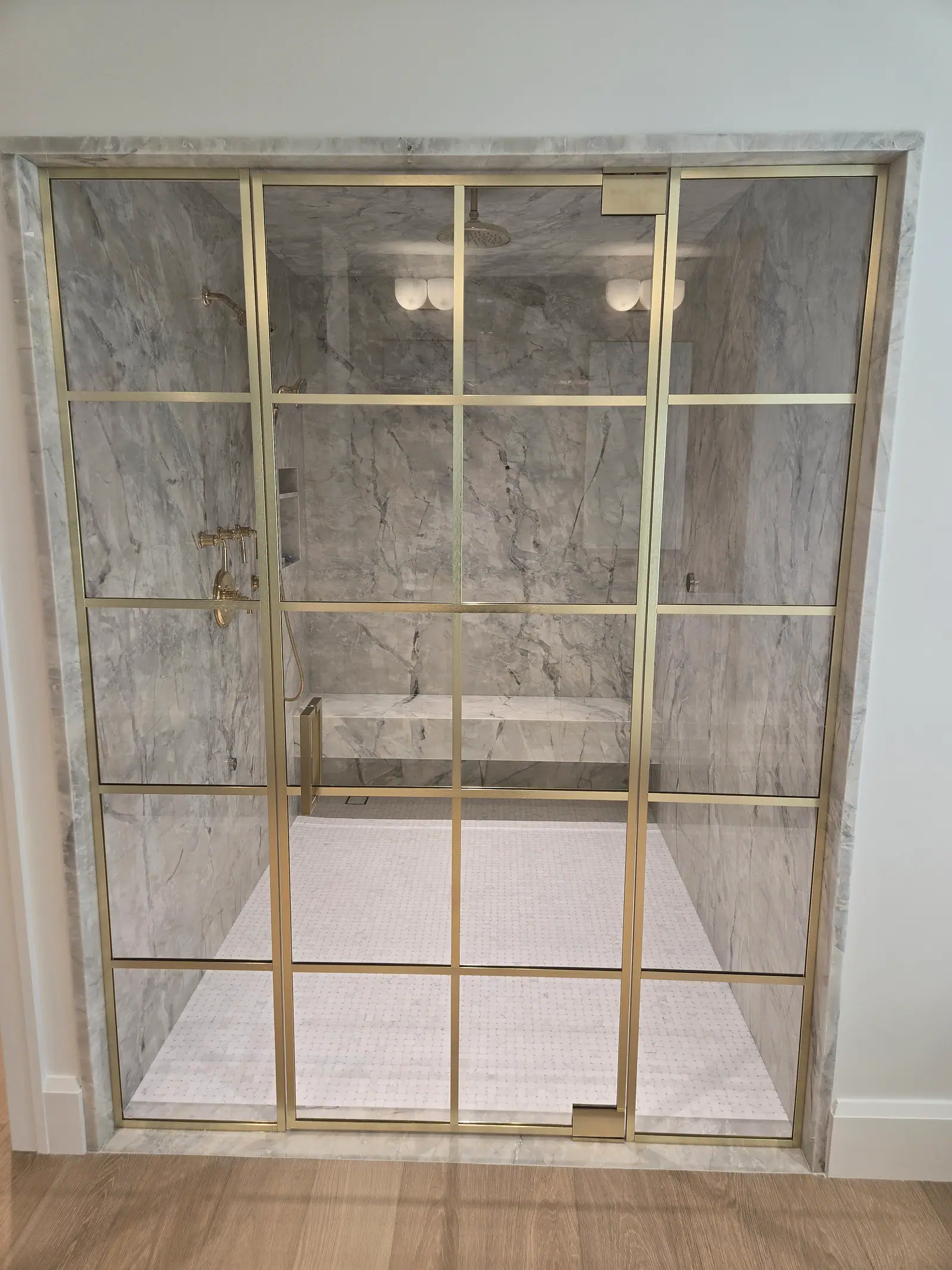 Brass grid glass shower enclosure framed in quartzite with a slab shower and bench inside