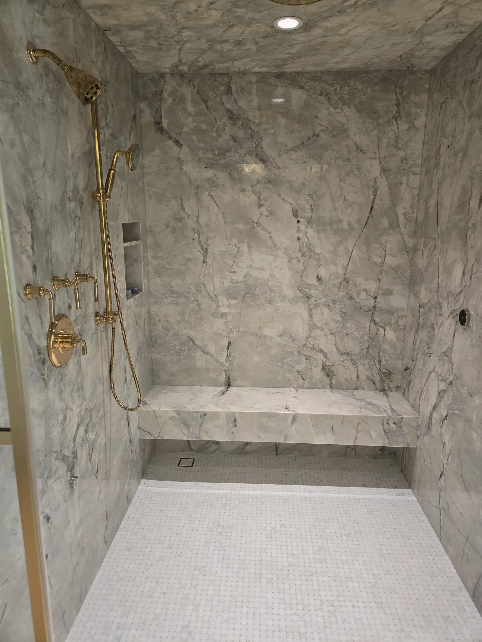 Quartzite slab shower with polished brass fixtures, floating bench, wall niche and basketweave mosaic floor