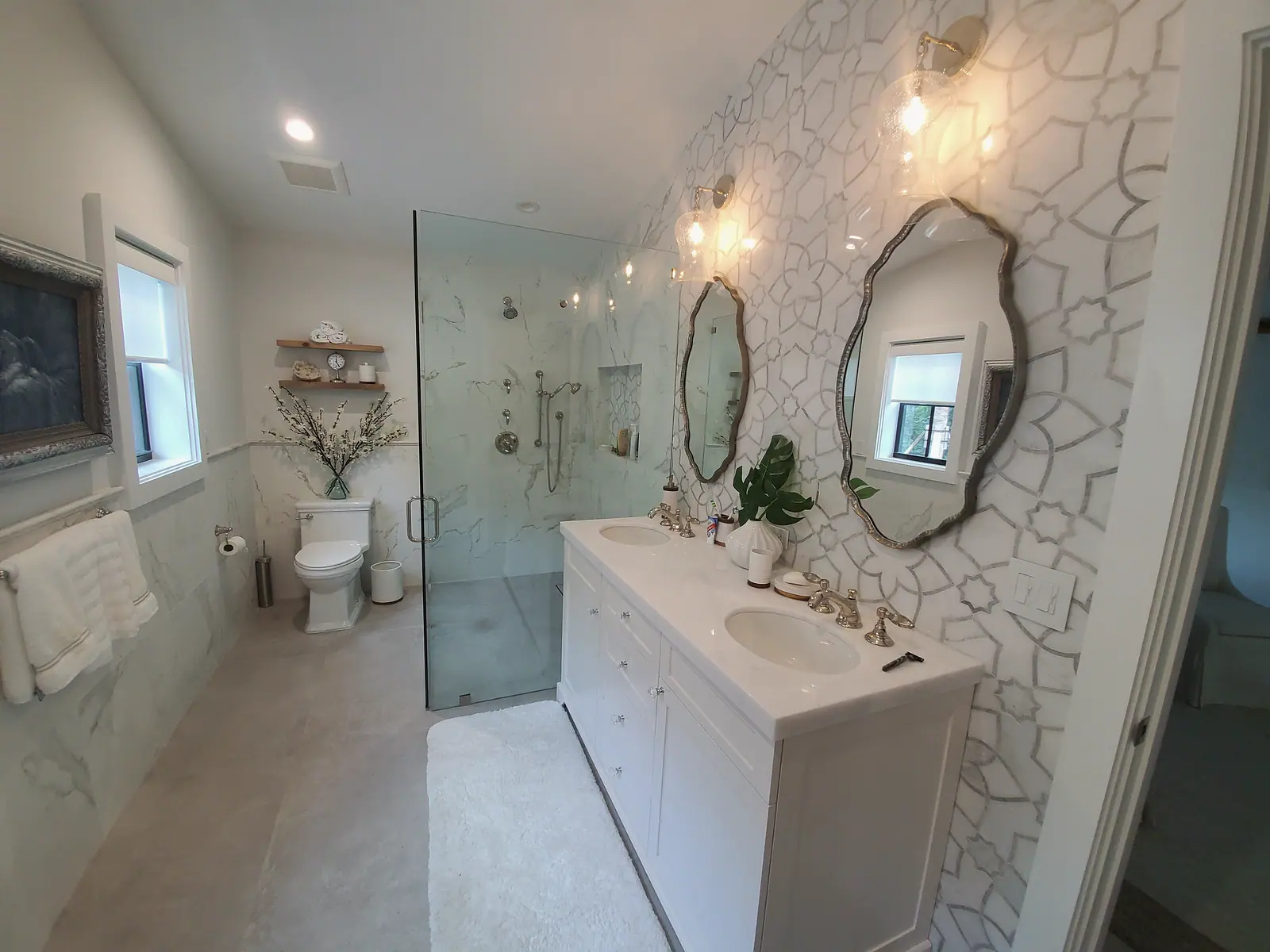 Bath with white double vanity, patterned marble mosaic wall, scalloped mirrors and frameless glass shower