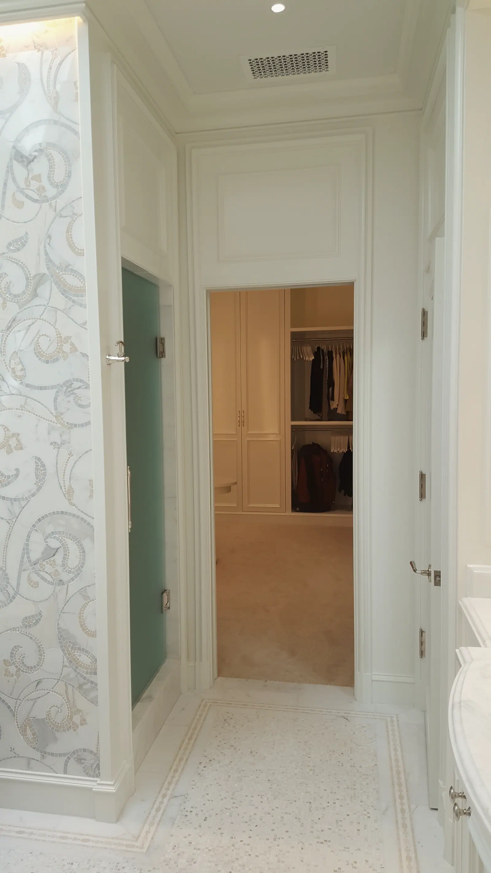 Paneled bath passage with mosaic accent wall, frosted shower door and marble mosaic floor leading to a walk-in closet