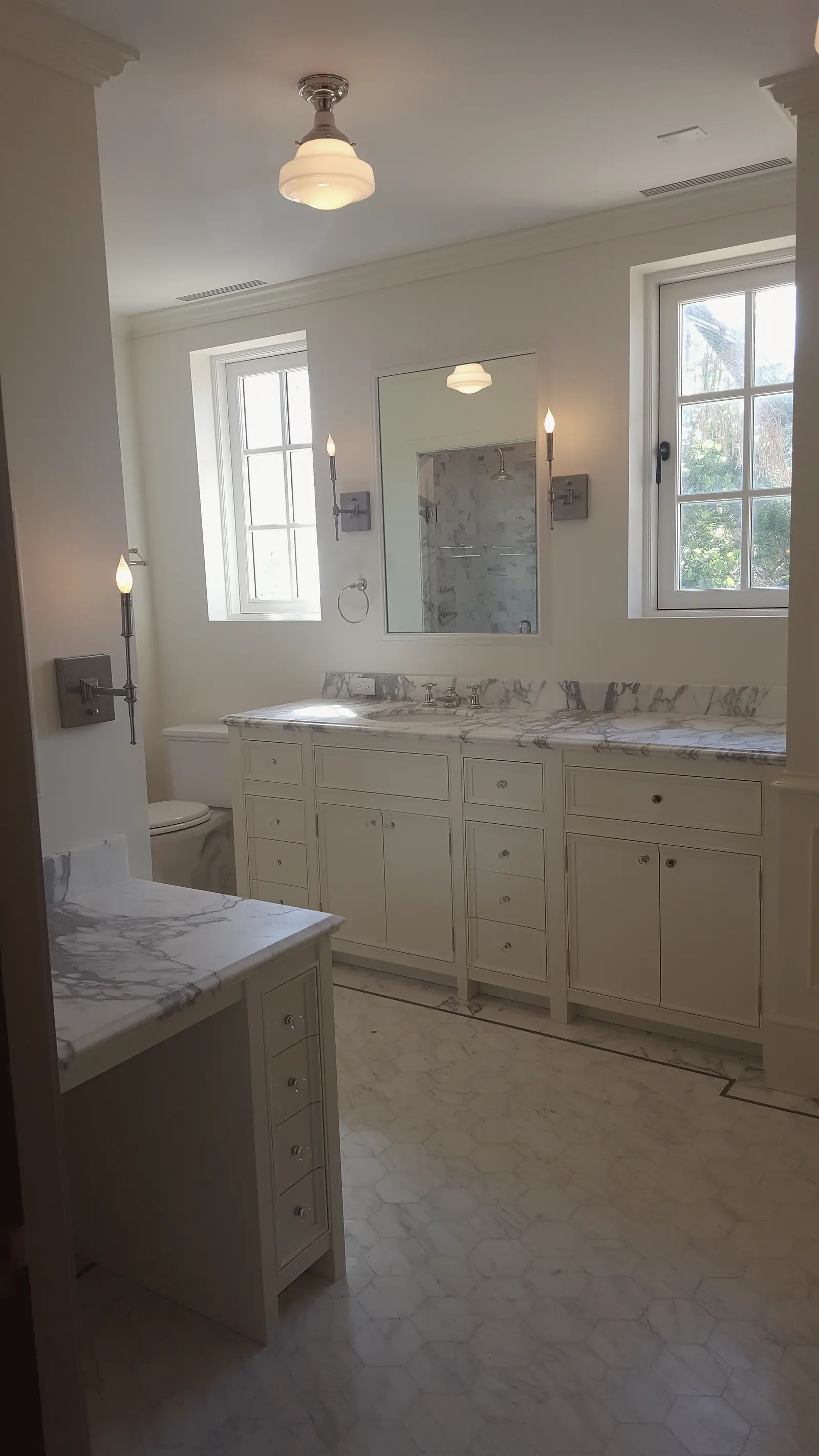 White double vanity with marble top, makeup desk, candle sconces and marble hexagon floor