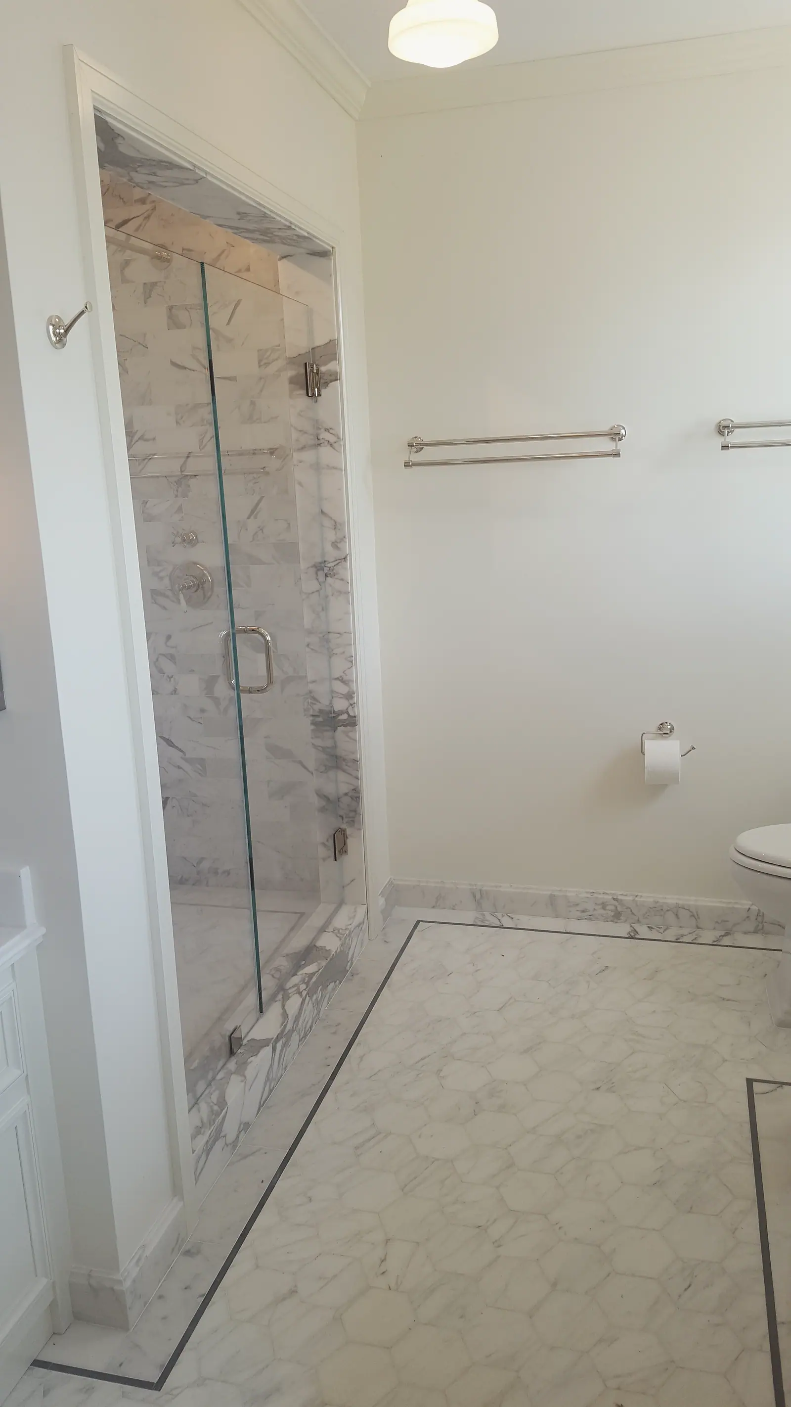 Frameless glass shower lined in marble beside a marble hexagon floor with a dark border inlay