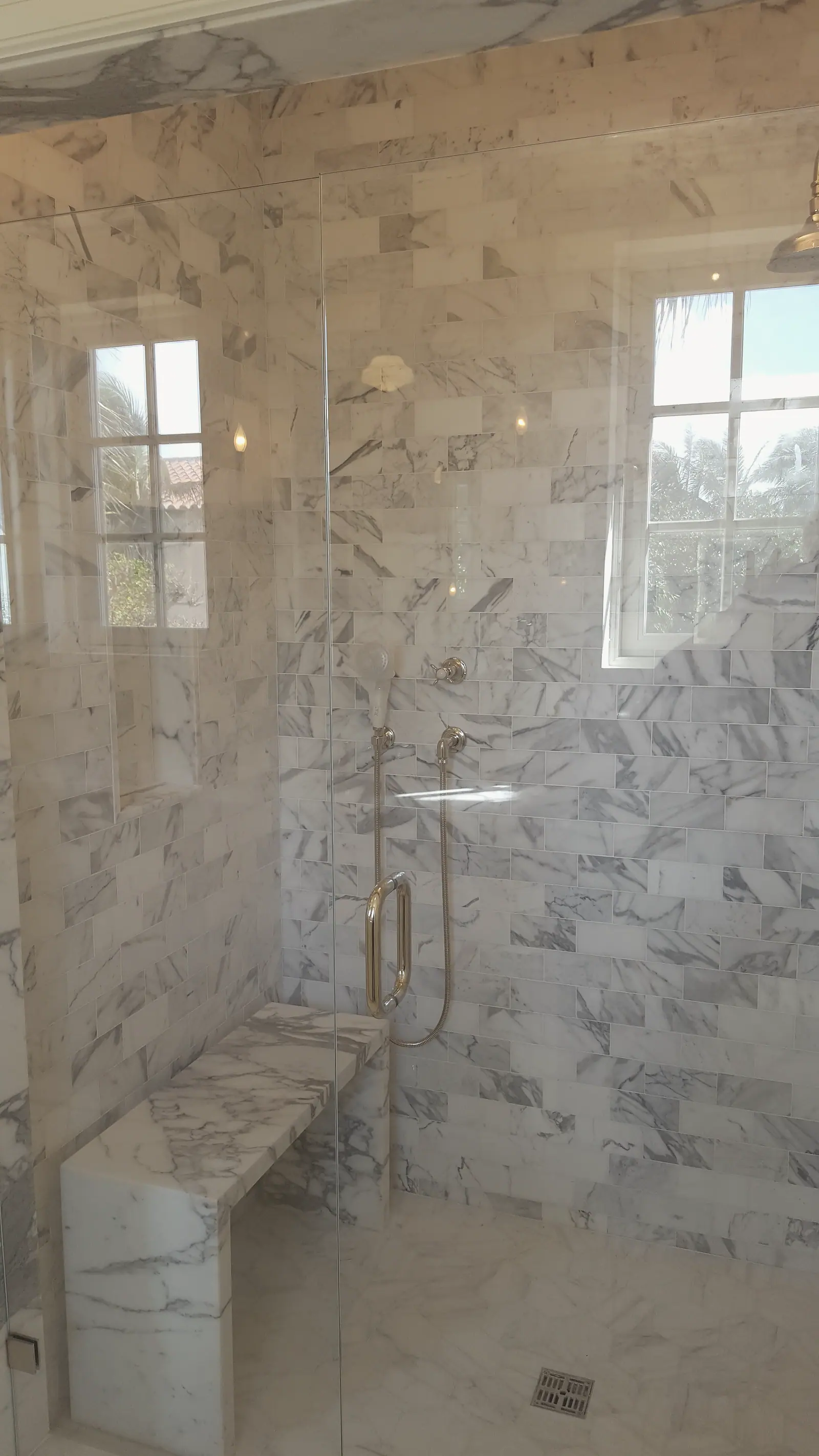 Marble tiled shower with slab bench, windows and polished nickel fixtures behind frameless glass