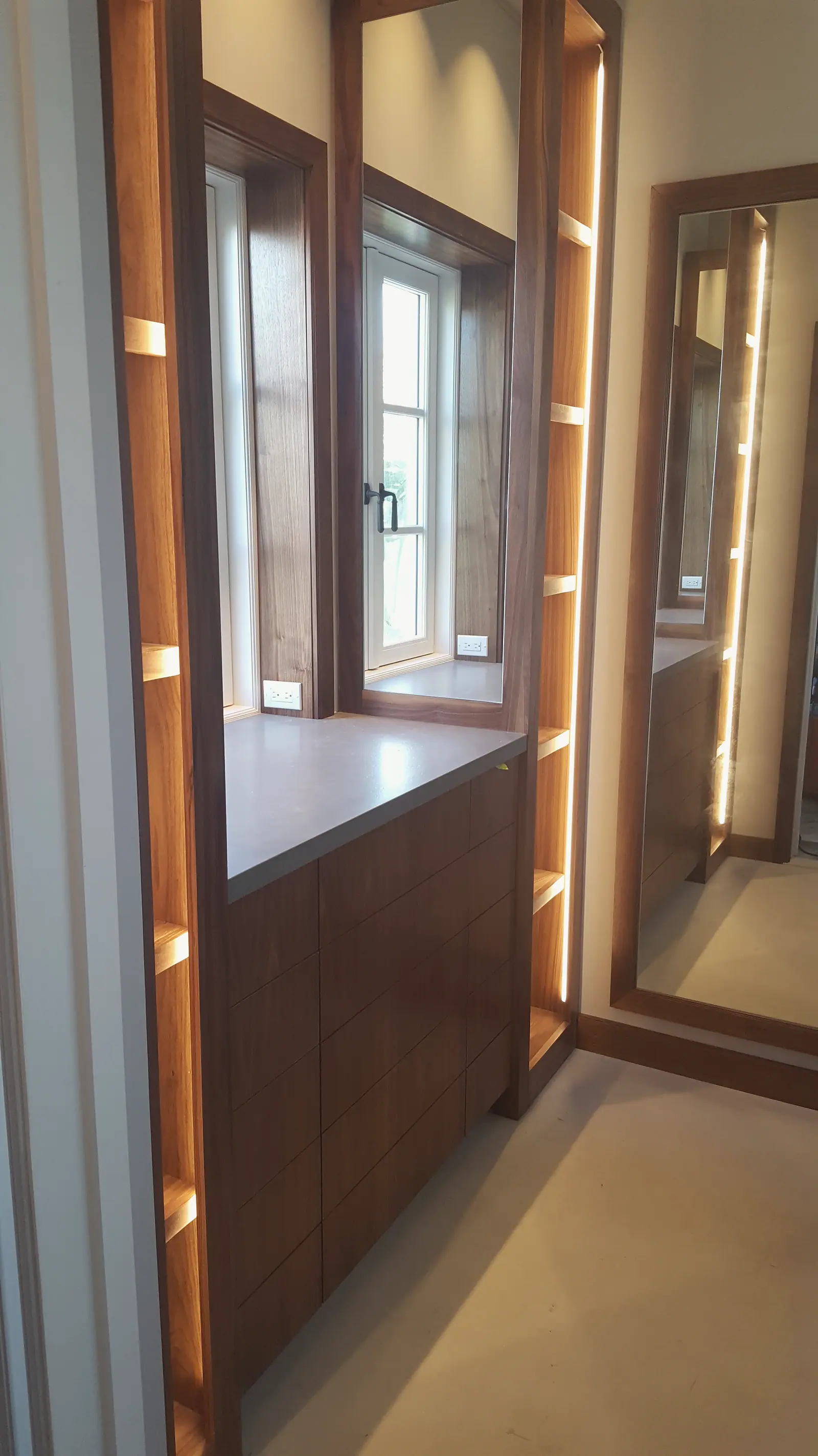 Walnut dressing room built-ins with lit open shelves, stone counter over drawers and tall framed mirror