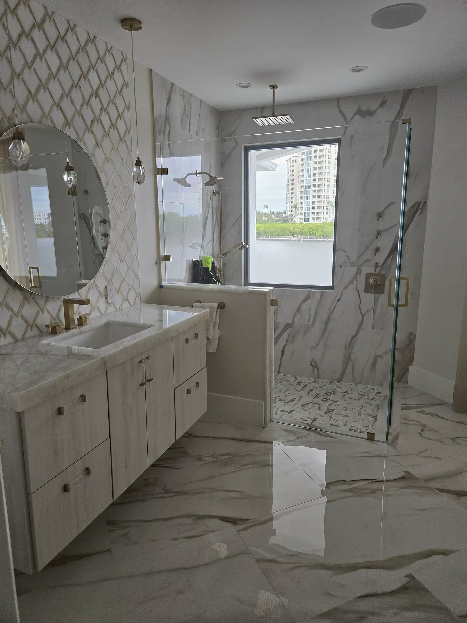 Floating vanity with quartzite top and brass fixtures beside a frameless marble walk-in shower with a rain head