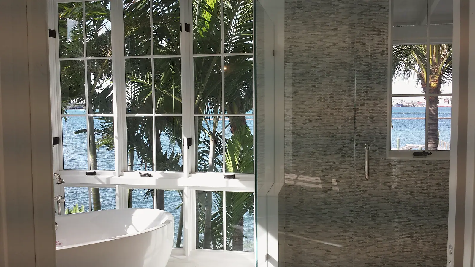 Soaking tub at water view windows next to a glass shower lined with marble mosaic tile