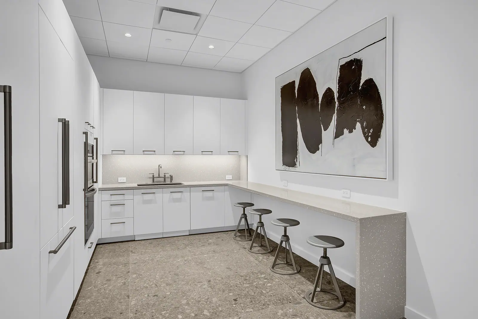 Office pantry with flat white cabinetry, terrazzo floor, quartz counter with stools and a large abstract painting