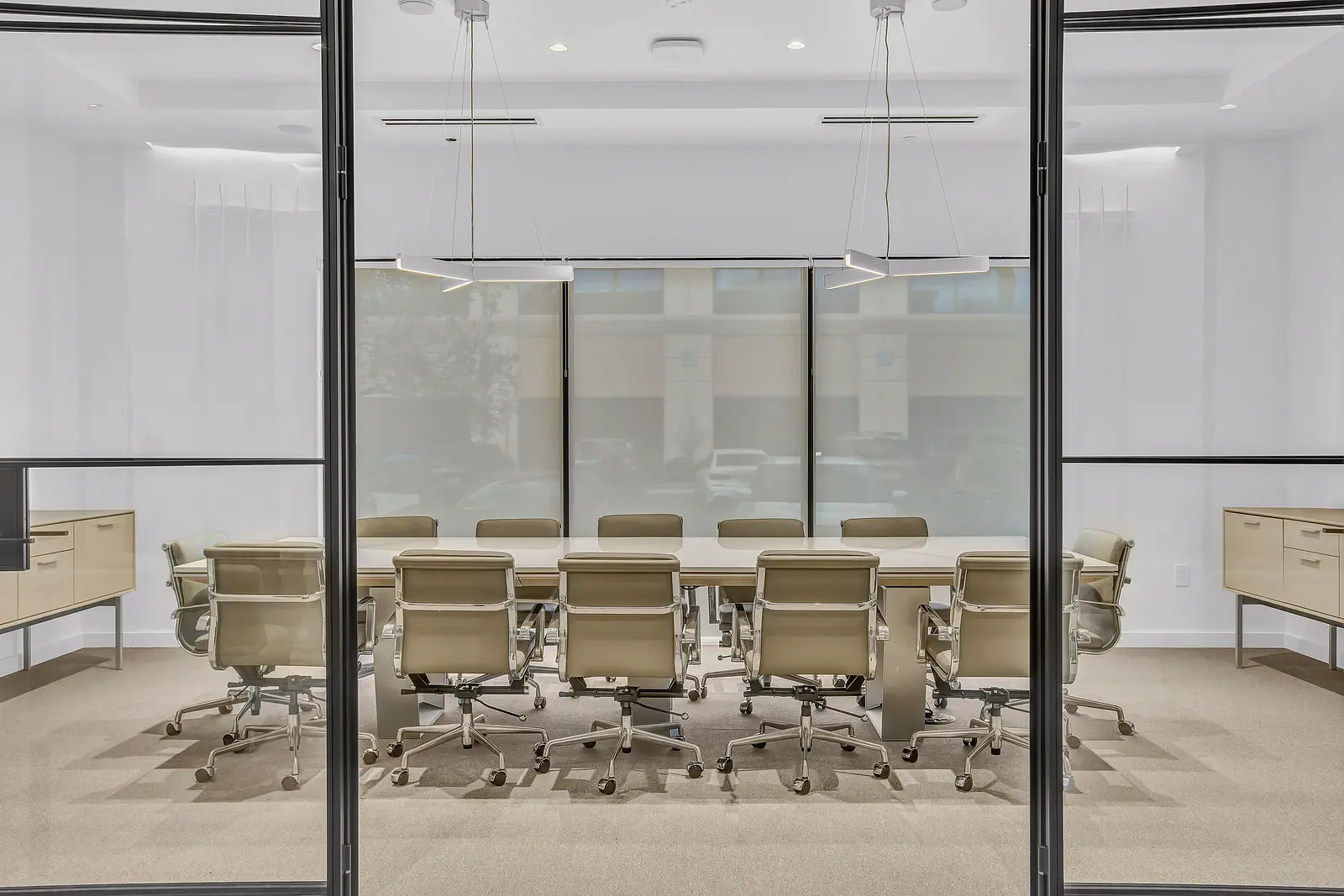 Conference room with a long table, leather chairs and linear pendants seen through steel framed glass doors
