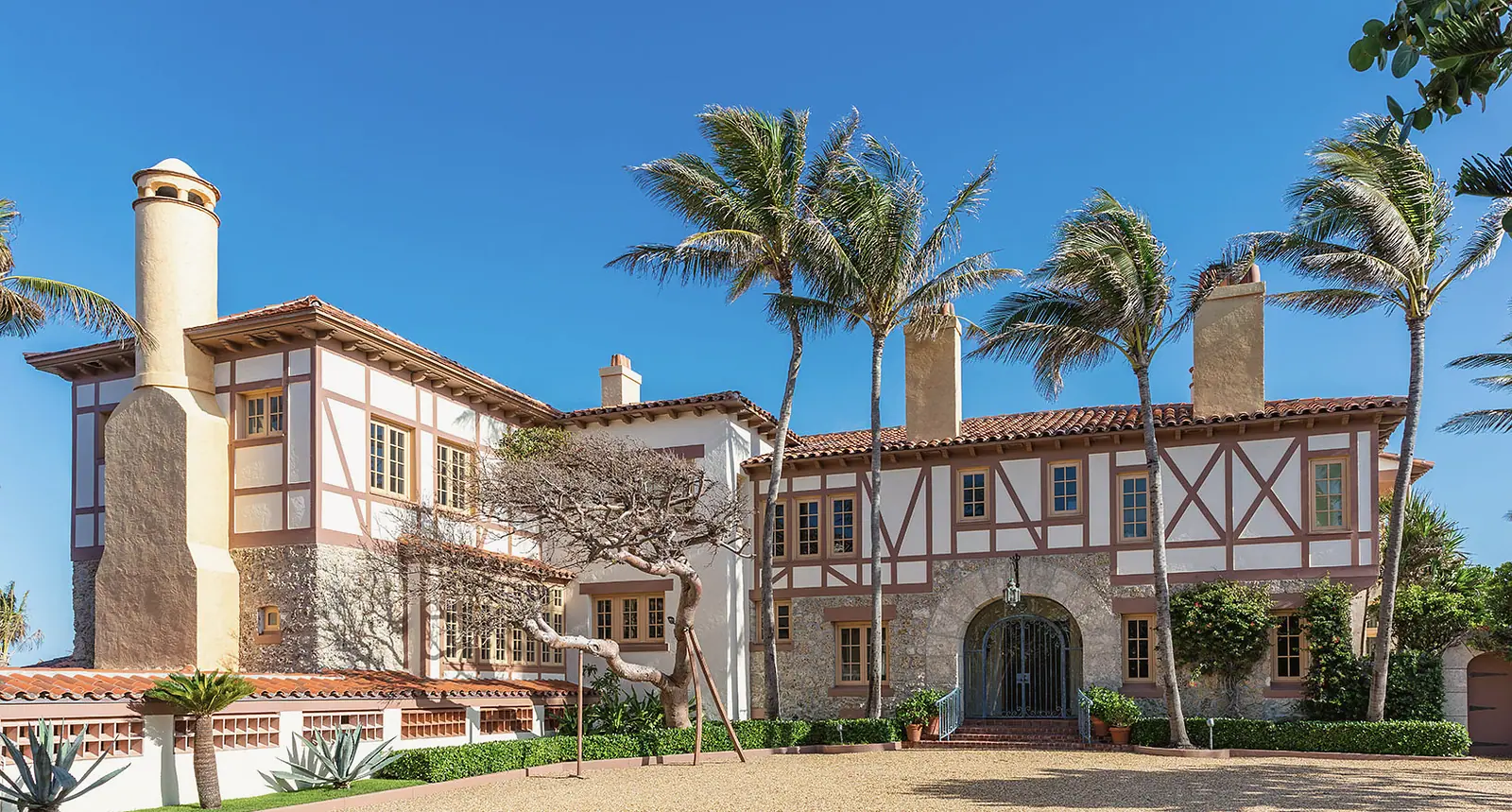 Half-timbered Mediterranean estate with a coquina stone entry, a wrought iron gate and tall palms