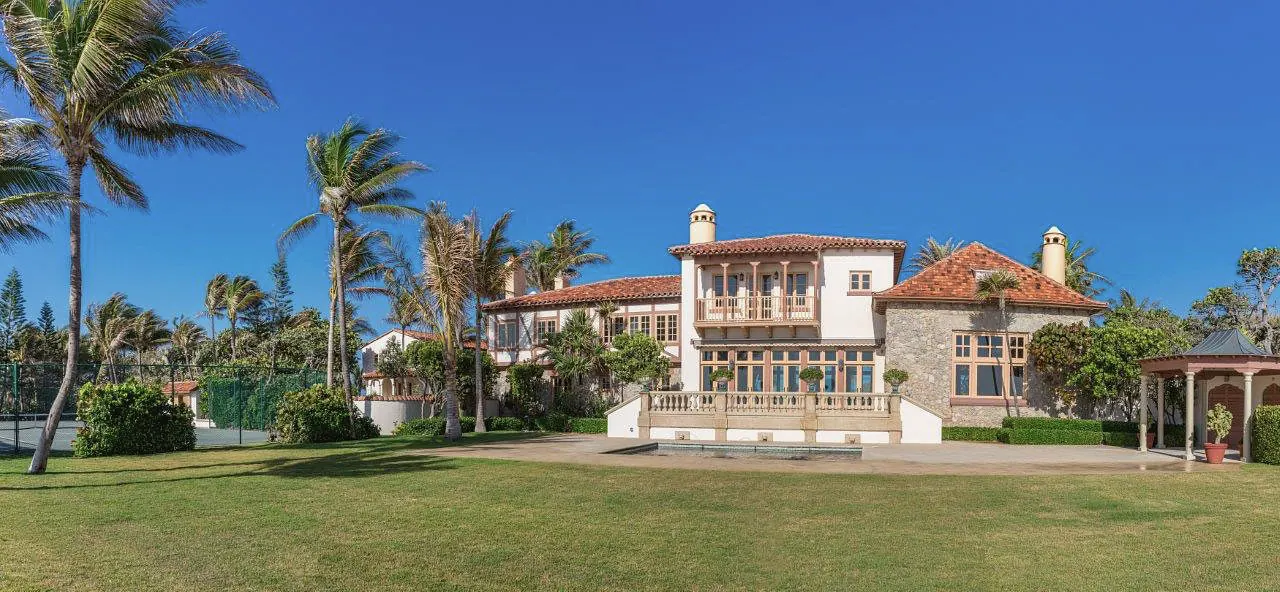 Estate seen across a wide lawn lined with palms