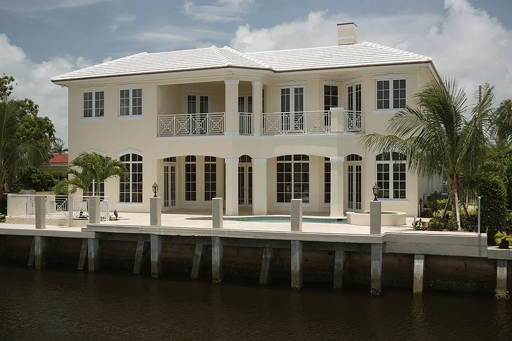 White two-story waterfront house with a long balcony over the seawall