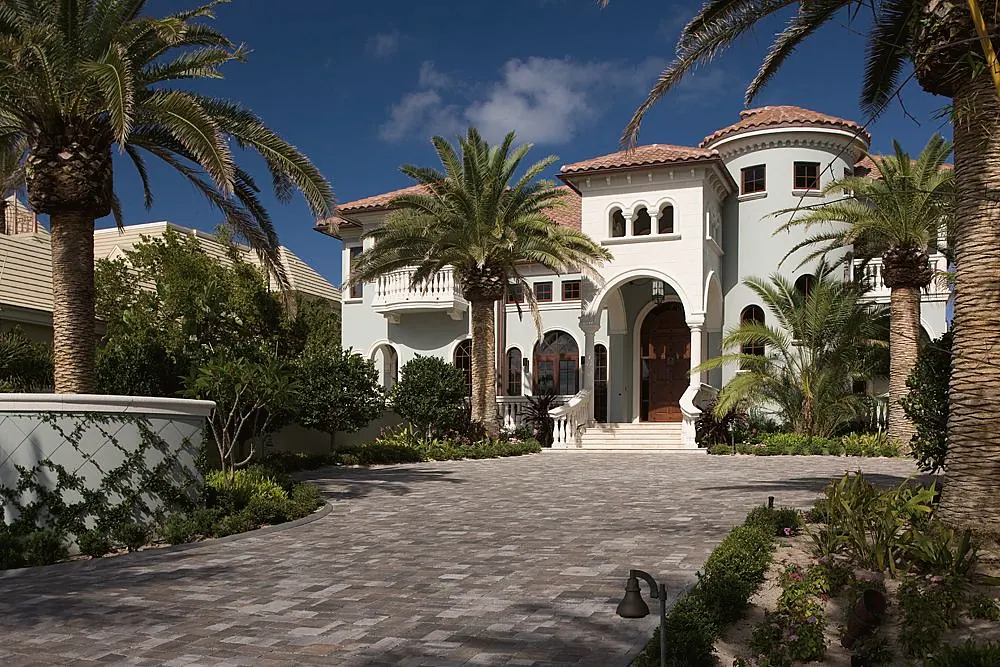 Mediterranean house with a round tower and an arched entry over a paver motor court, among palms