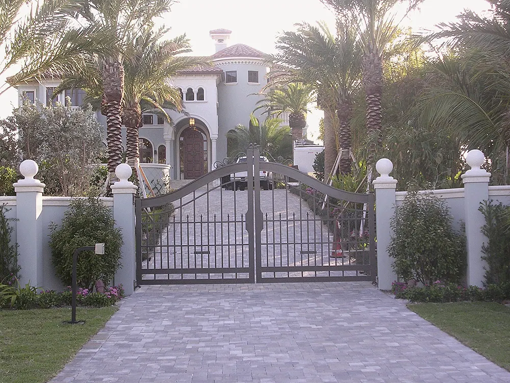 Iron gate across a paver drive, the house beyond among palms