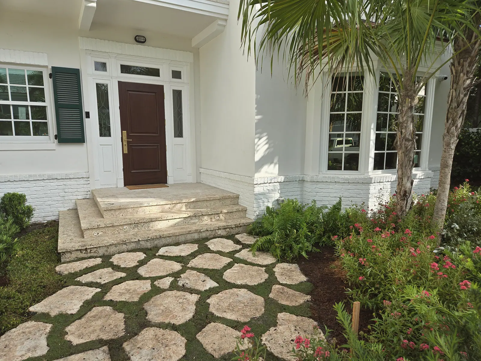 Front entry with a mahogany door, white trim, coral stone steps and stone pavers set in grass