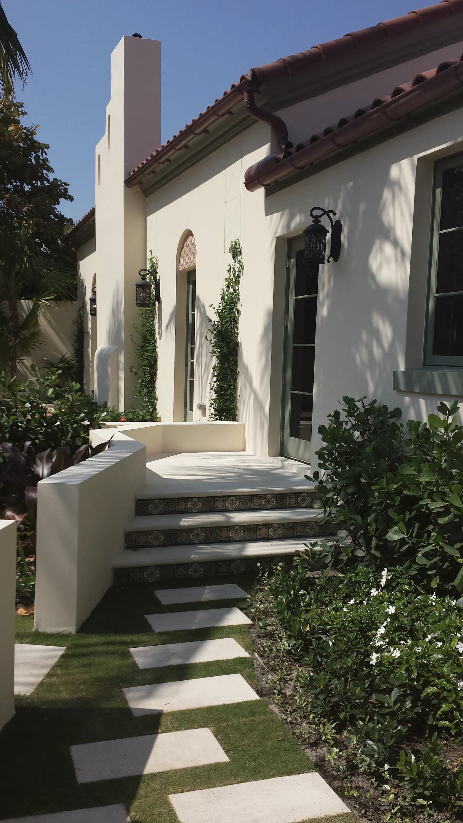 Stucco courtyard entry with iron lanterns, arched doorway, tile riser steps and limestone stepping stones set in lawn