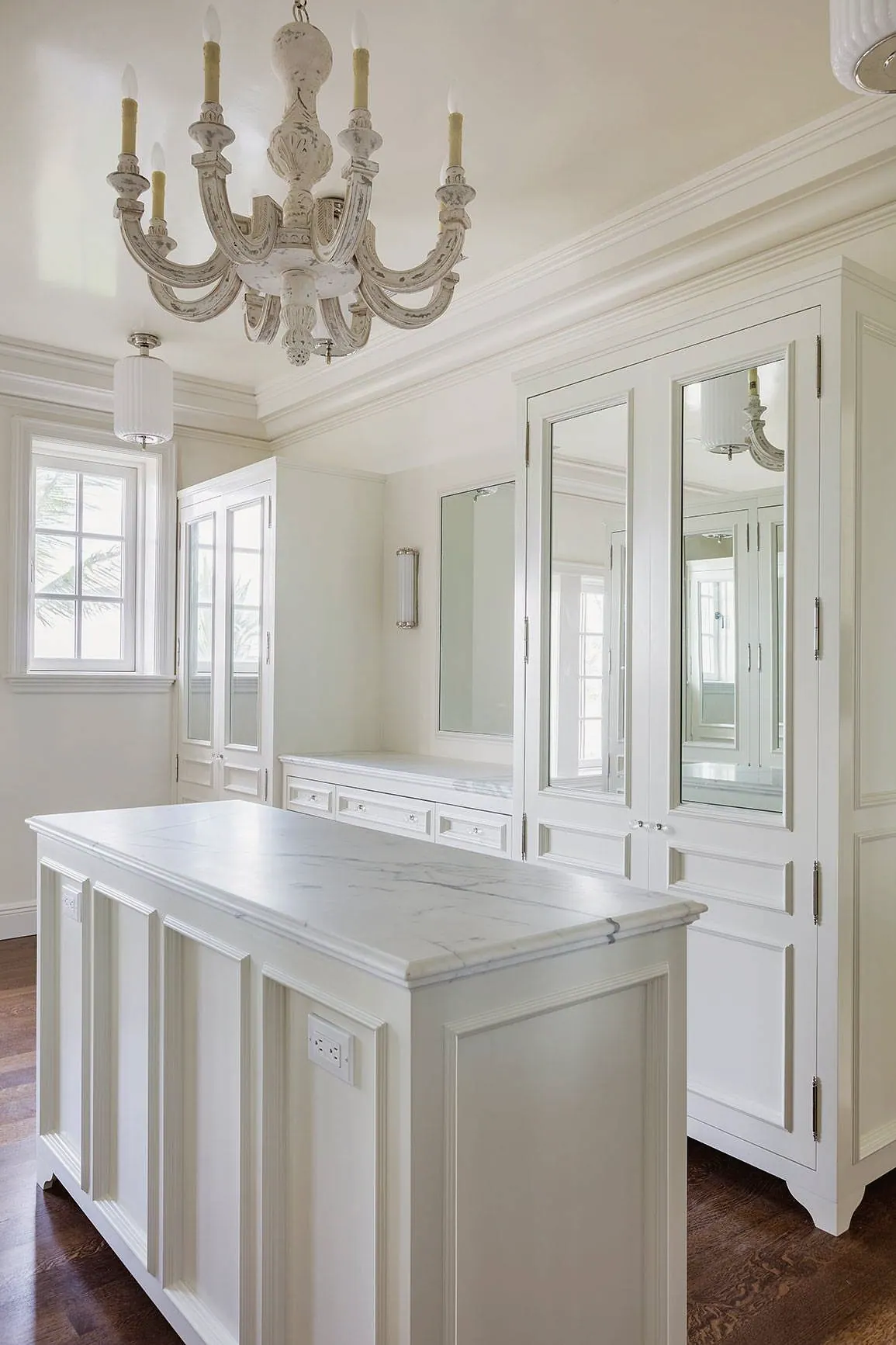 Dressing room with a marble-topped island, glass-front wardrobes and a chandelier