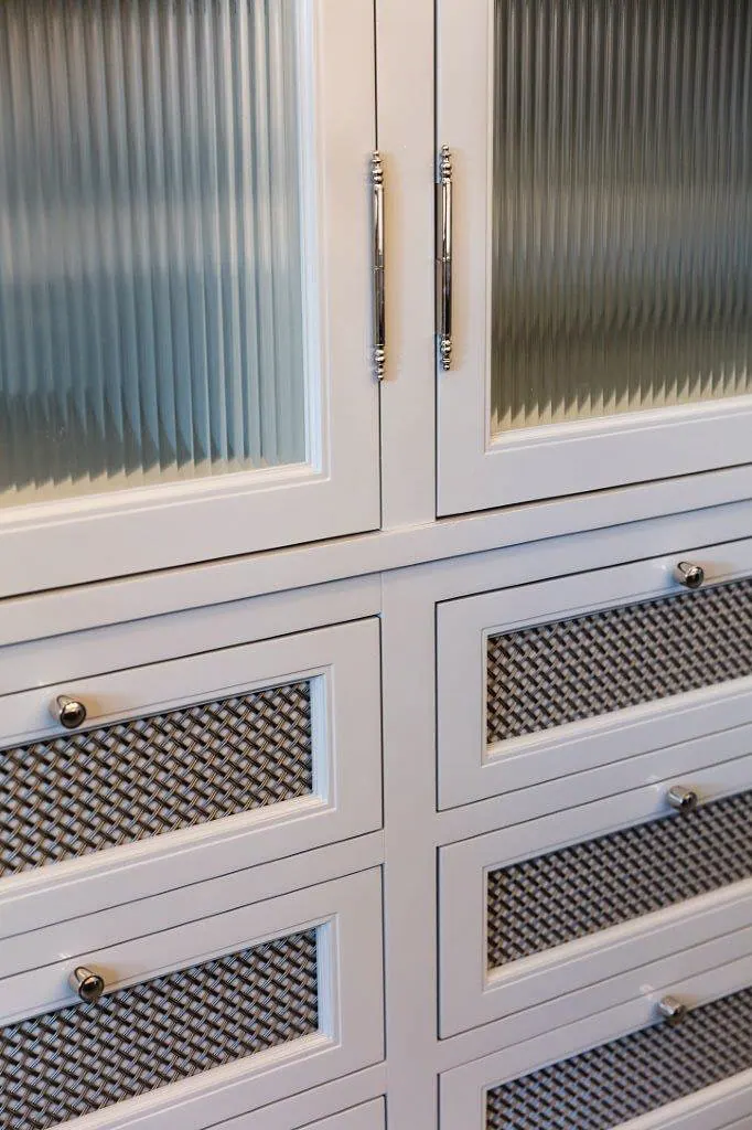 White cabinetry with reeded glass doors over drawers faced in woven metal