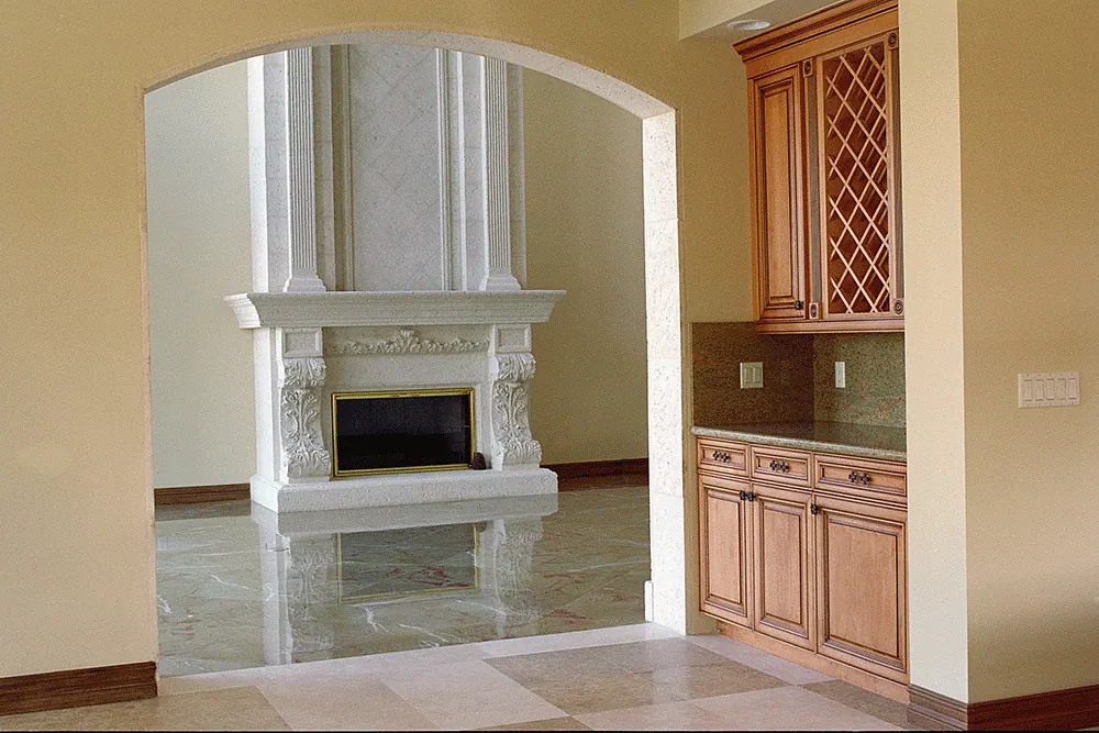 Carved stone fireplace seen through an arch, a wet bar with a wine lattice beside it