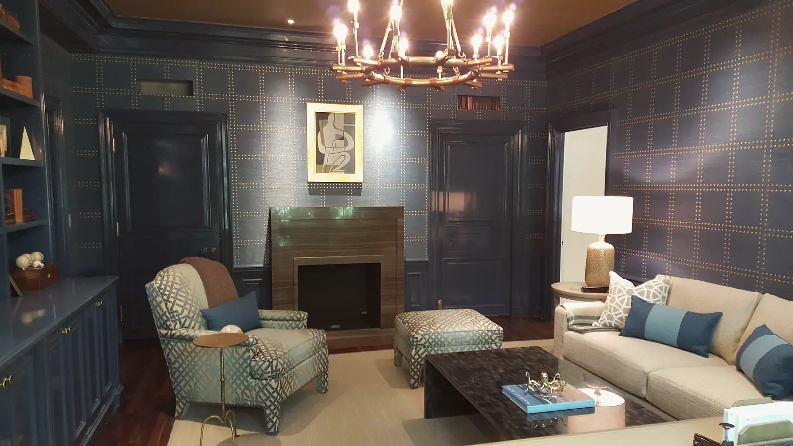 Navy library with nailhead grasscloth walls, lacquered paneled doors and a stone fireplace surround