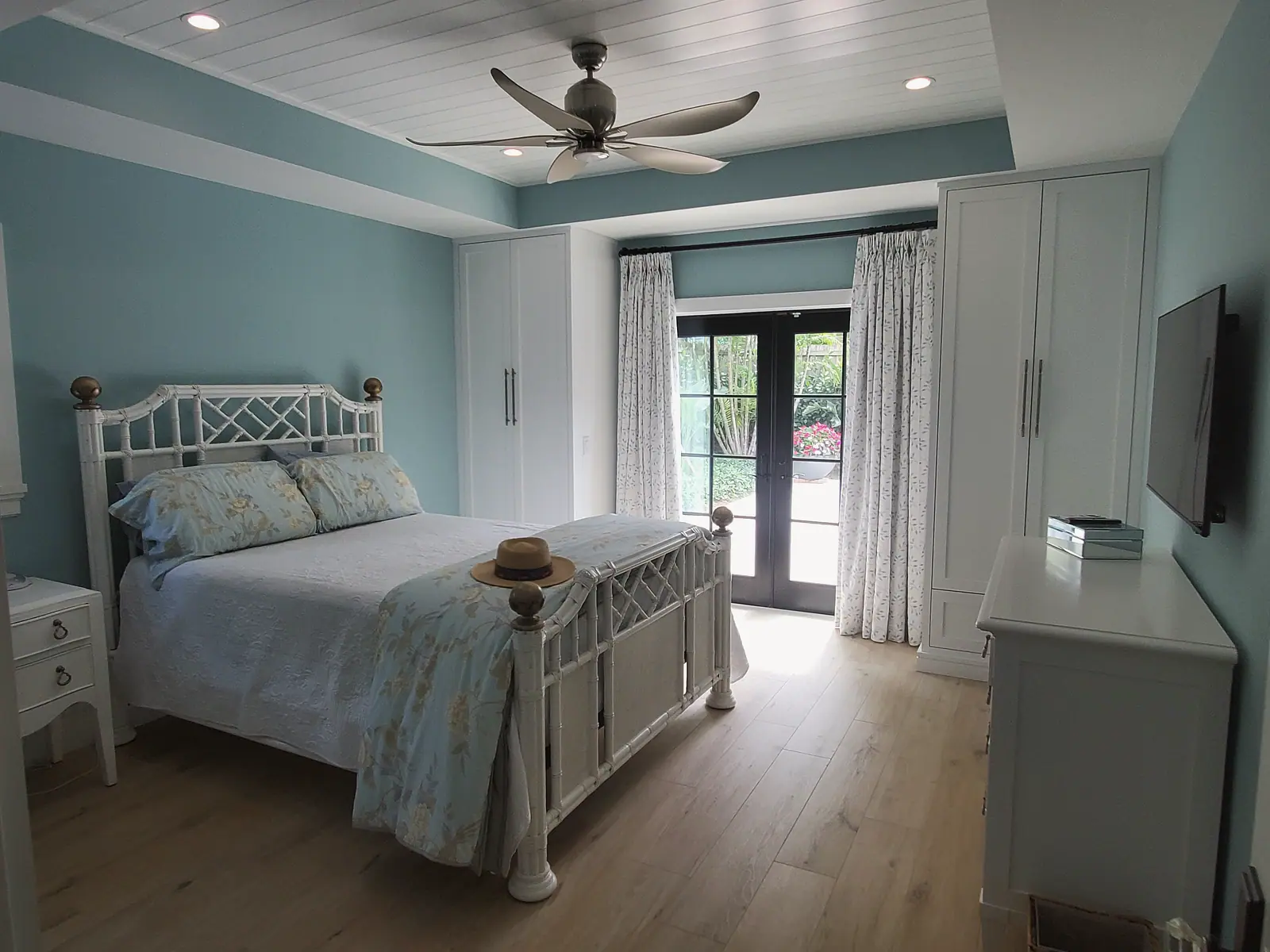 Bedroom with white plank tray ceiling, built-in wardrobes, wood floor and French doors to a garden