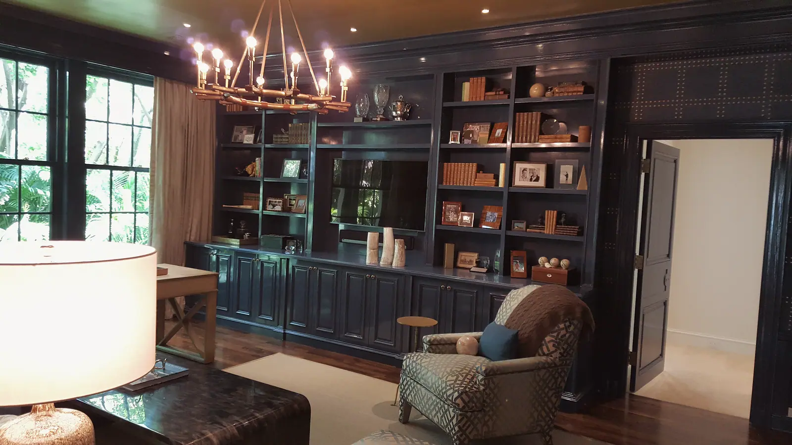Navy lacquered library with built-in bookcases and cabinets under a brass chandelier