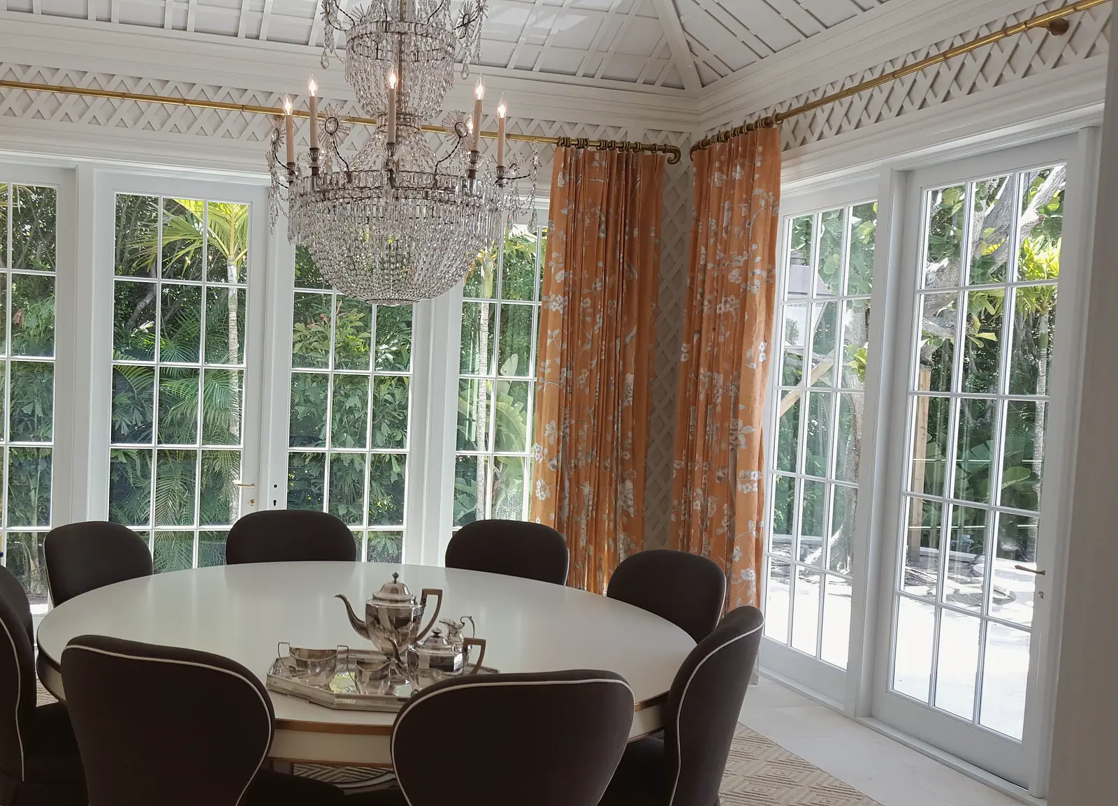 Garden room with white lattice walls, crystal chandelier and round dining table before French doors