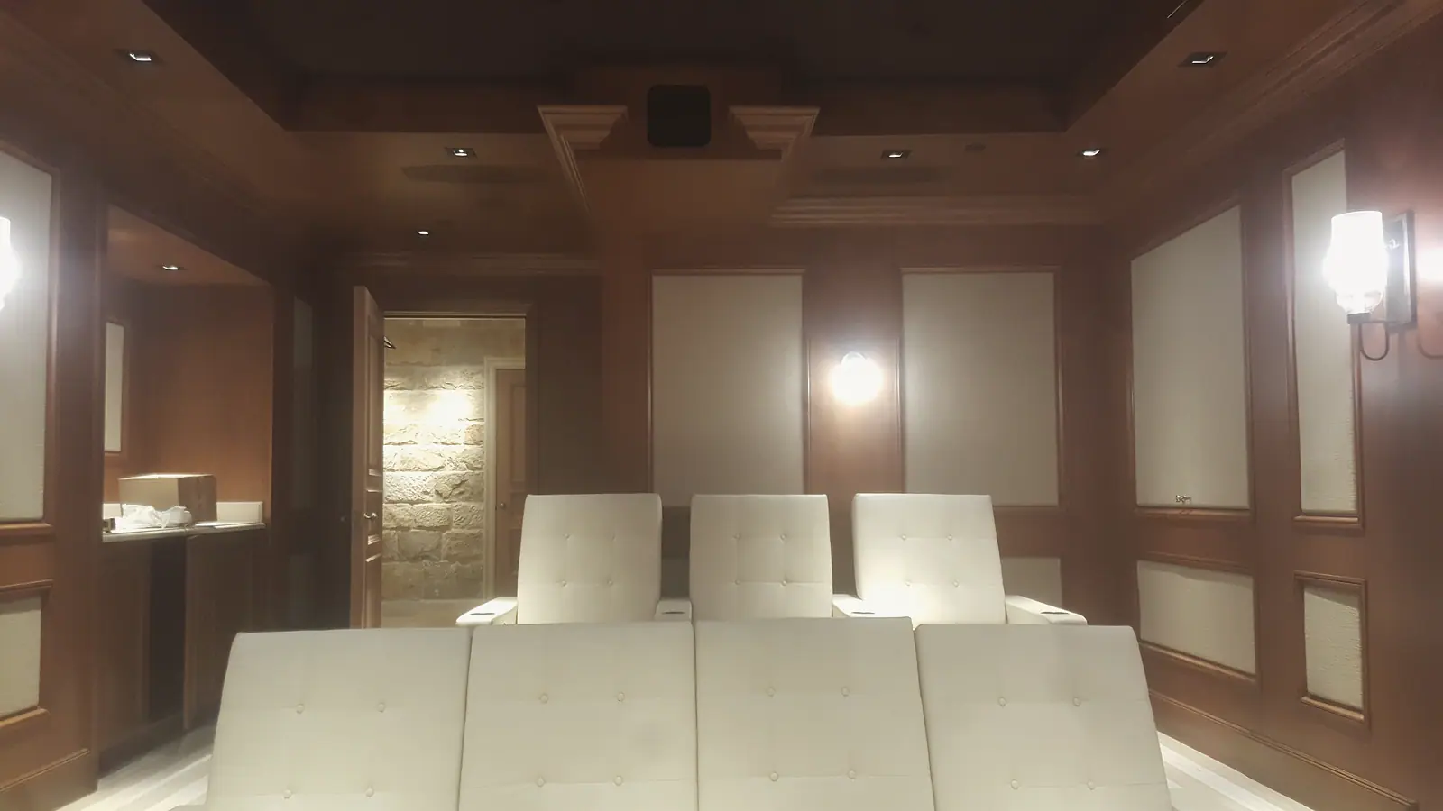Home theater rear wall with cherry paneling, fabric panels and tufted cream seating