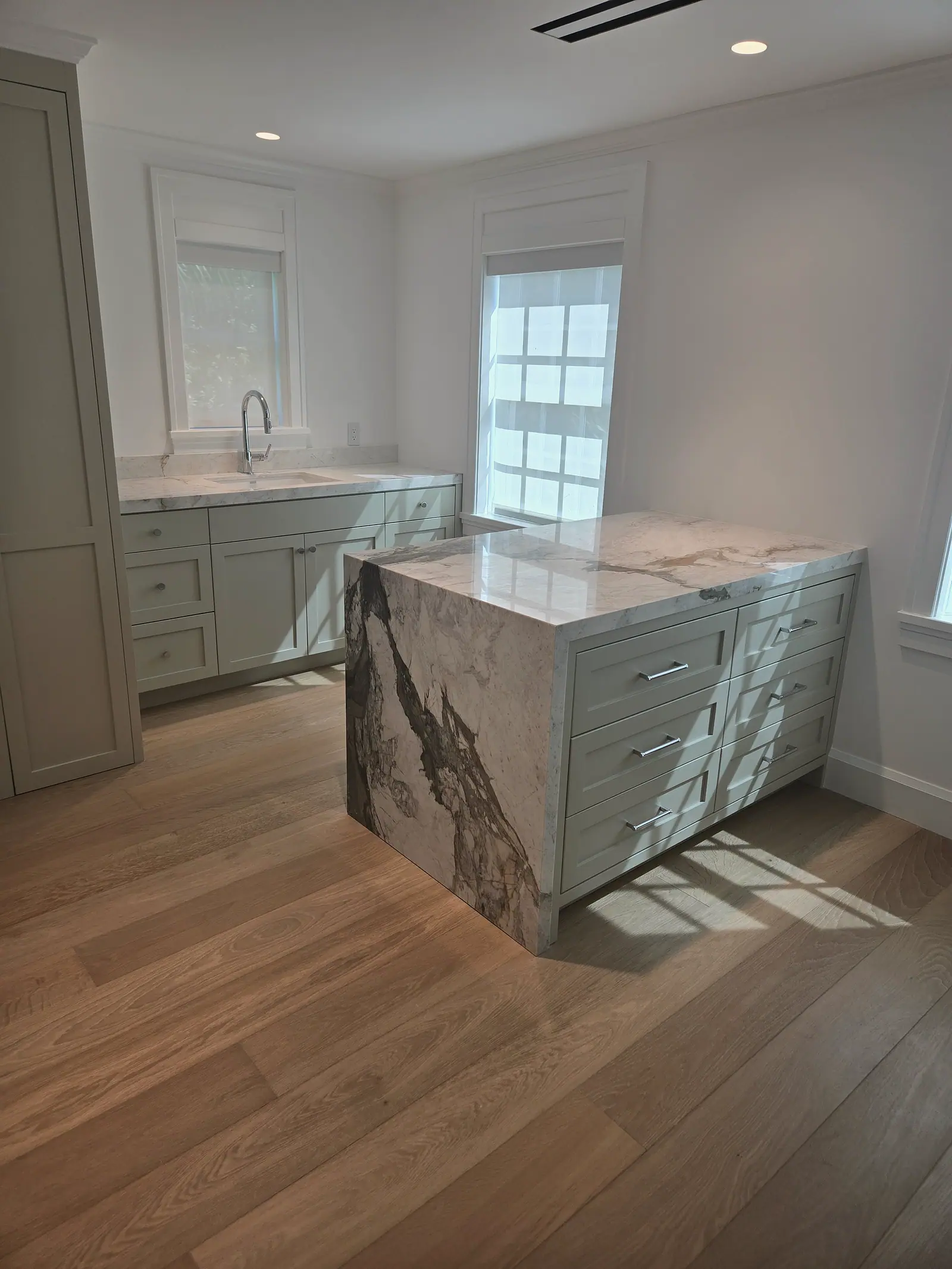 Sage green Shaker cabinets with a sink and a marble waterfall island with drawers on wide white oak floors