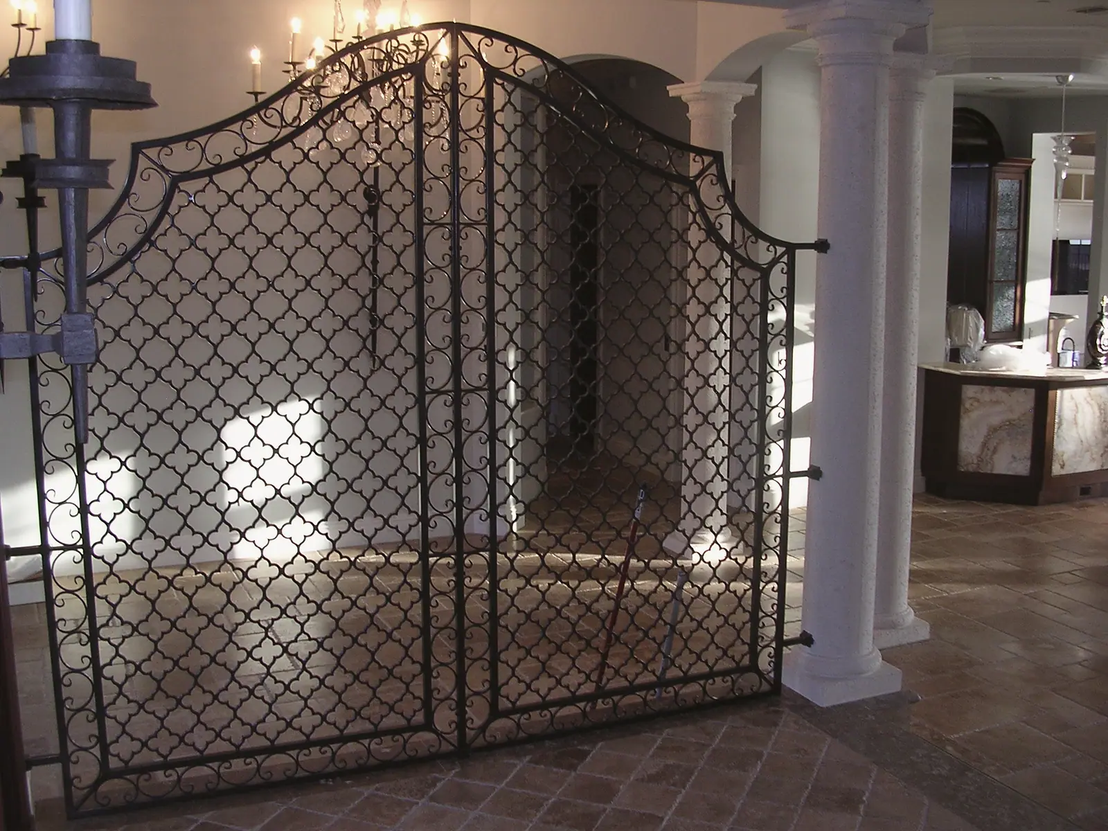 Arched wrought iron interior gates with a quatrefoil pattern beside cast stone columns on travertine floors