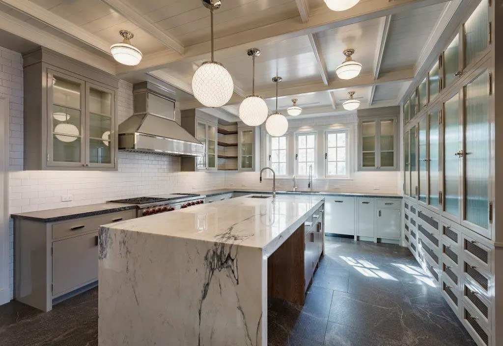 White kitchen with a marble waterfall island and glass-front cabinets