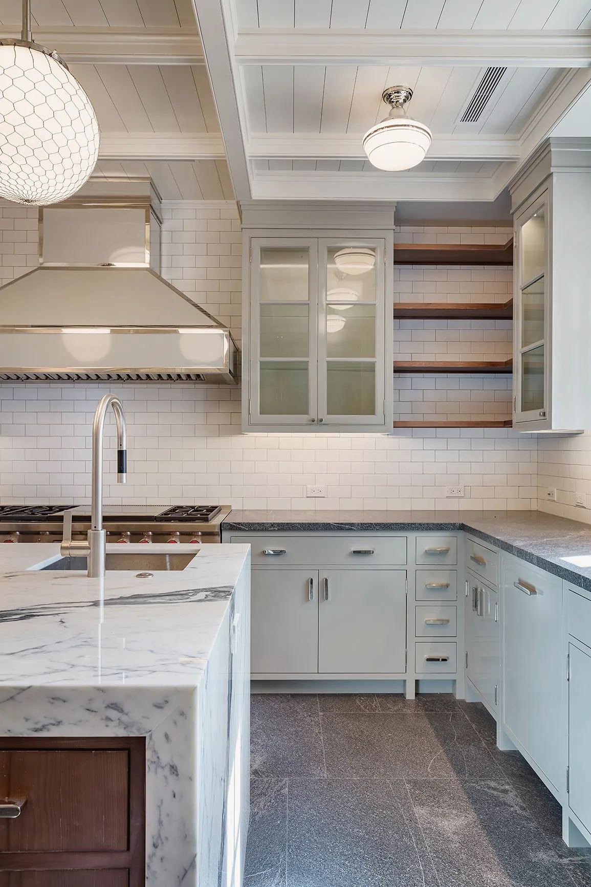 Marble counters, a hood and open shelving in a white kitchen