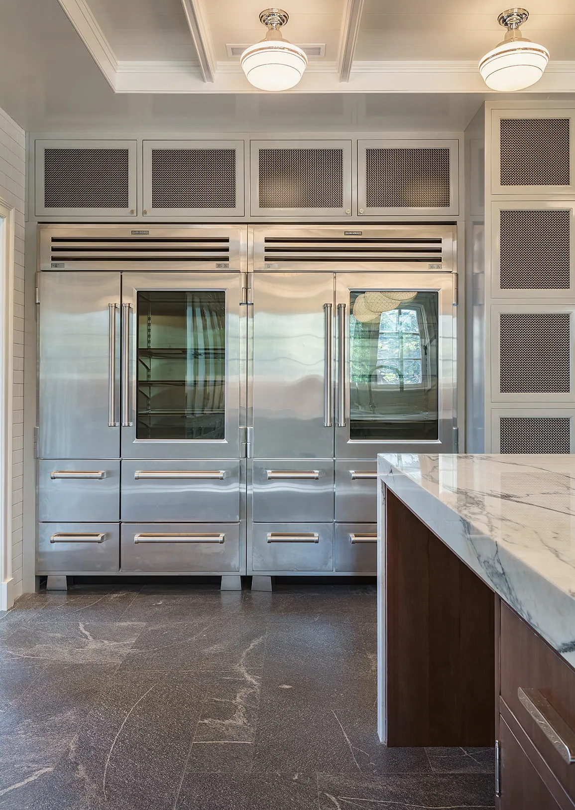 Paired built-in refrigerators beside a marble island