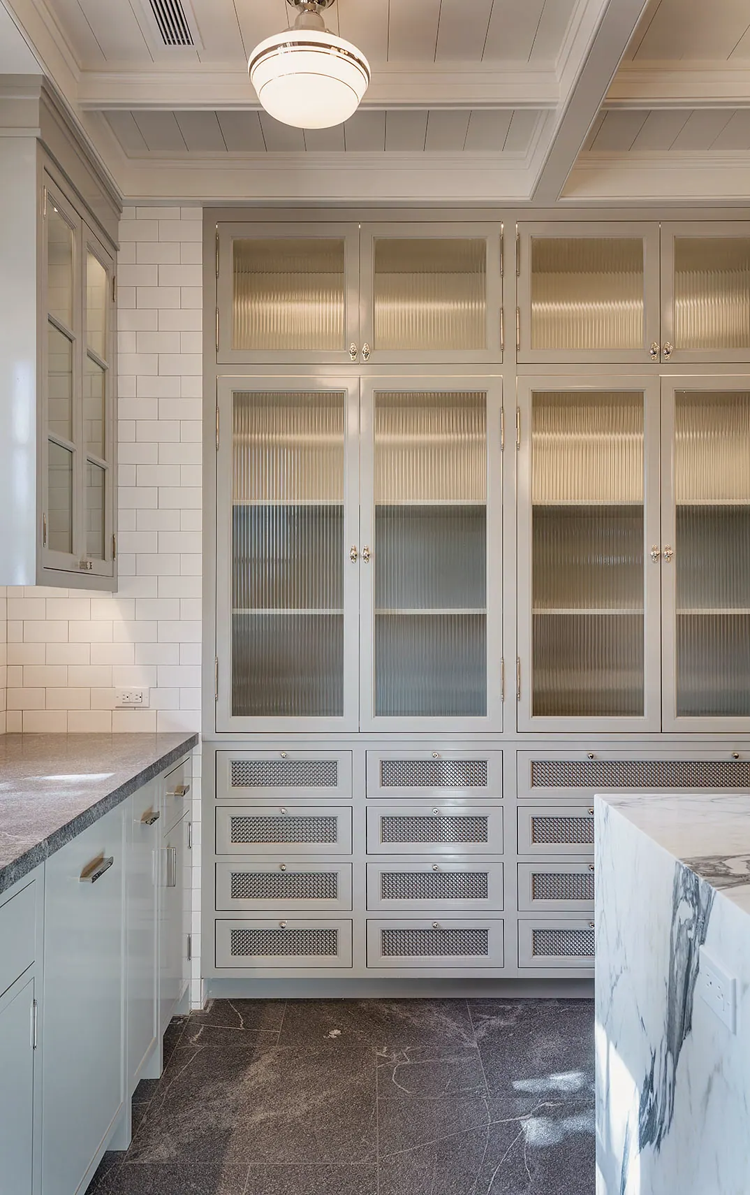 Wall of glass-front cabinets over drawers beside a marble island