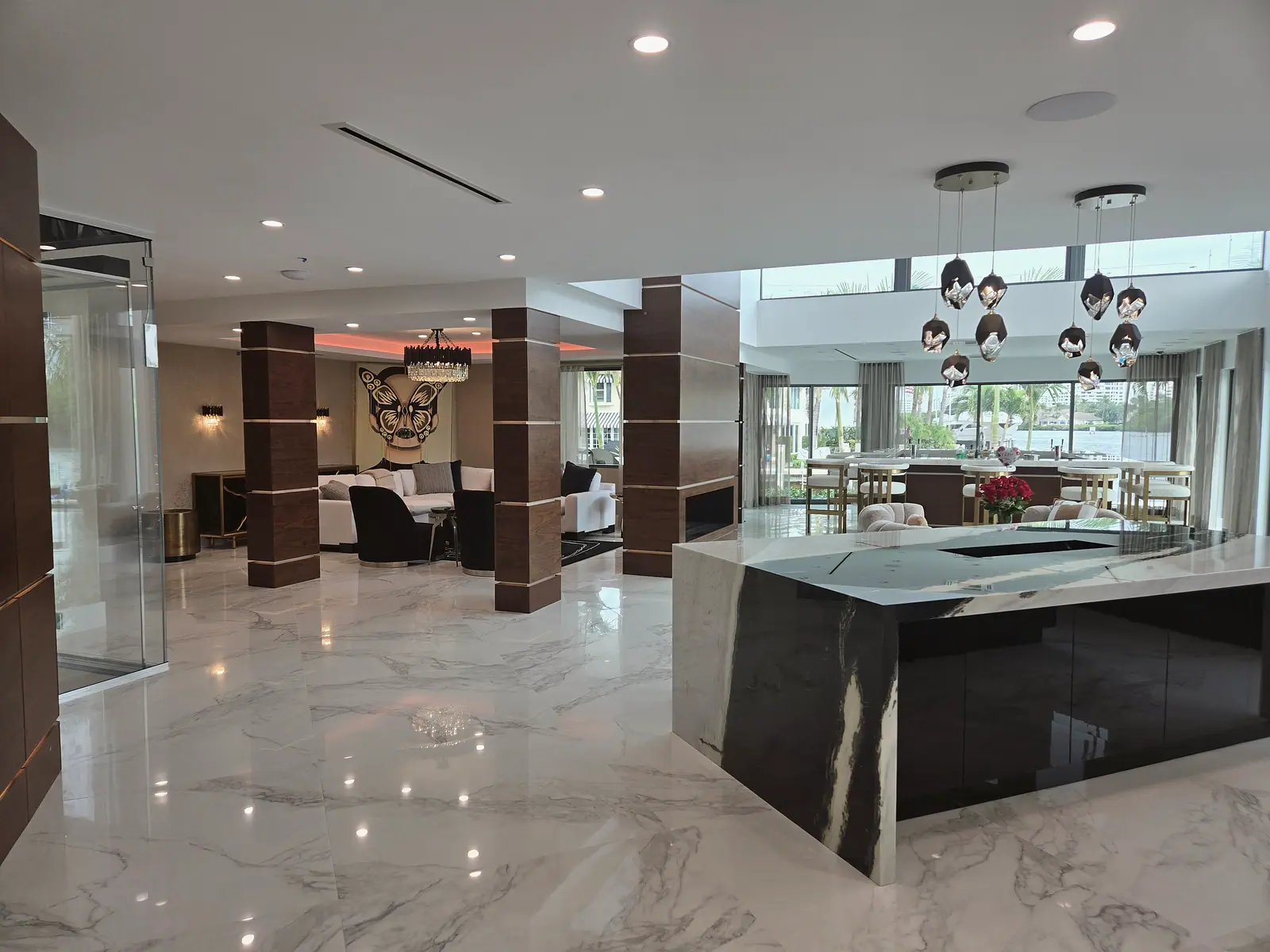 Open great room with a black and white stone waterfall island, walnut clad columns and sculptural pendant lights