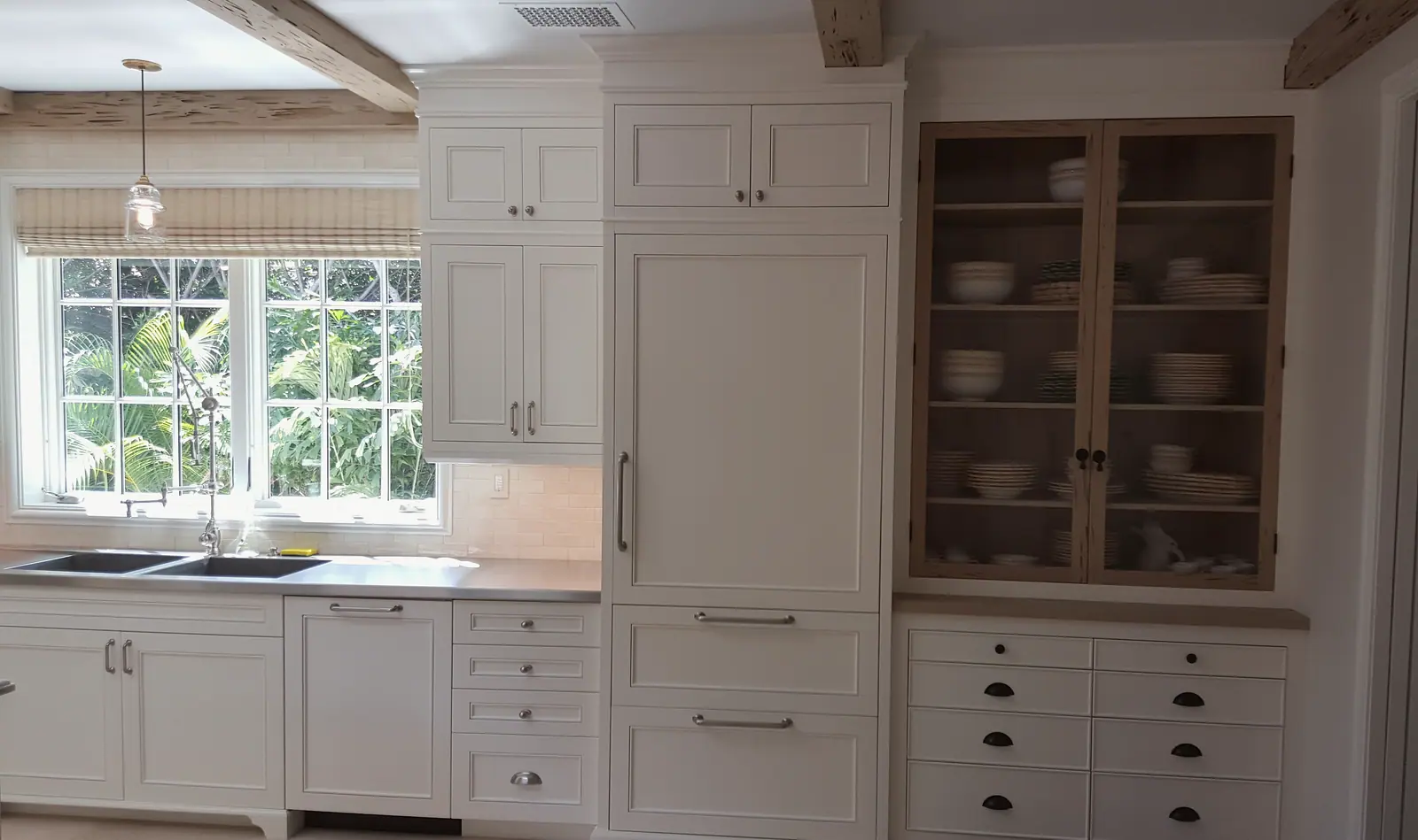 White inset kitchen cabinetry with a paneled refrigerator and a glass-front wood china cabinet beside a window over the sink