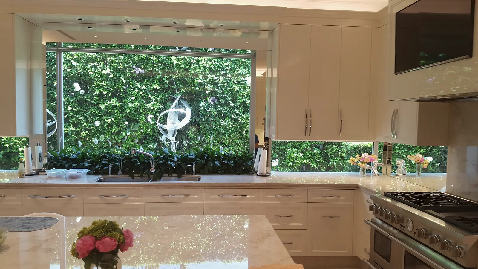 White kitchen sink wall with a large window framing a living green wall and a glass sculpture