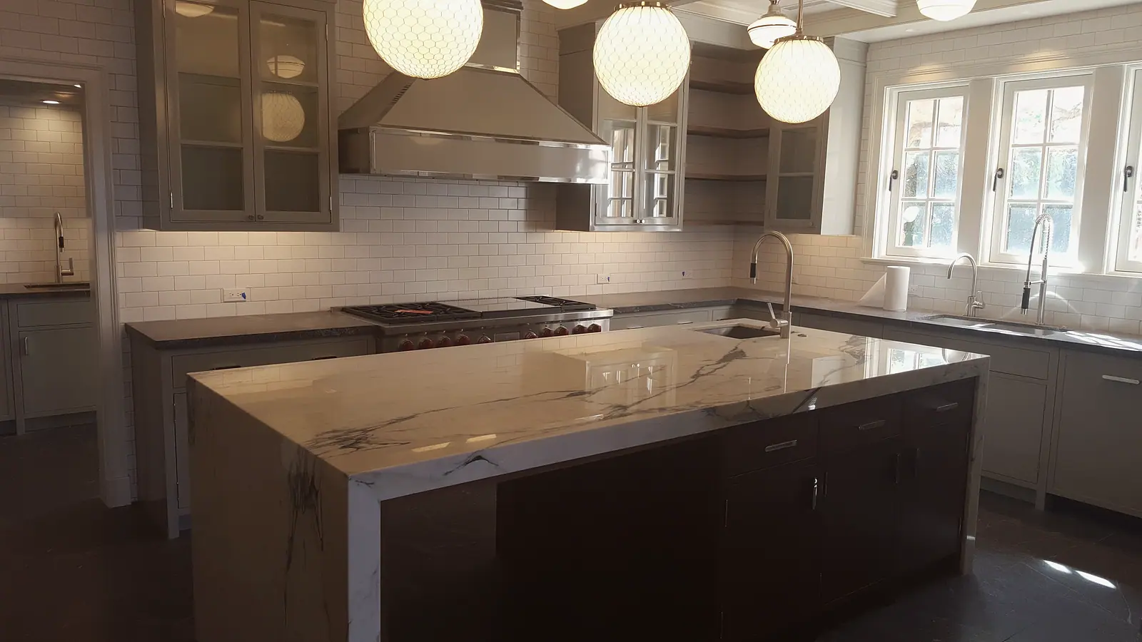 Kitchen with a waterfall marble island, gray inset cabinets, subway tile and globe pendants