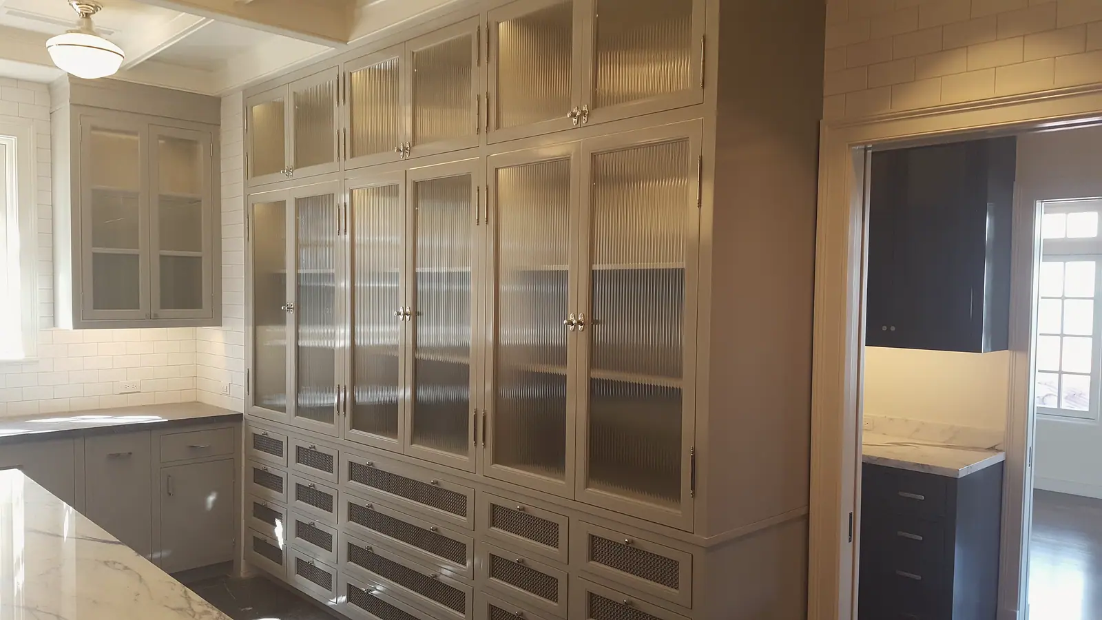 Floor to ceiling gray cabinetry with reeded glass doors and mesh front drawers