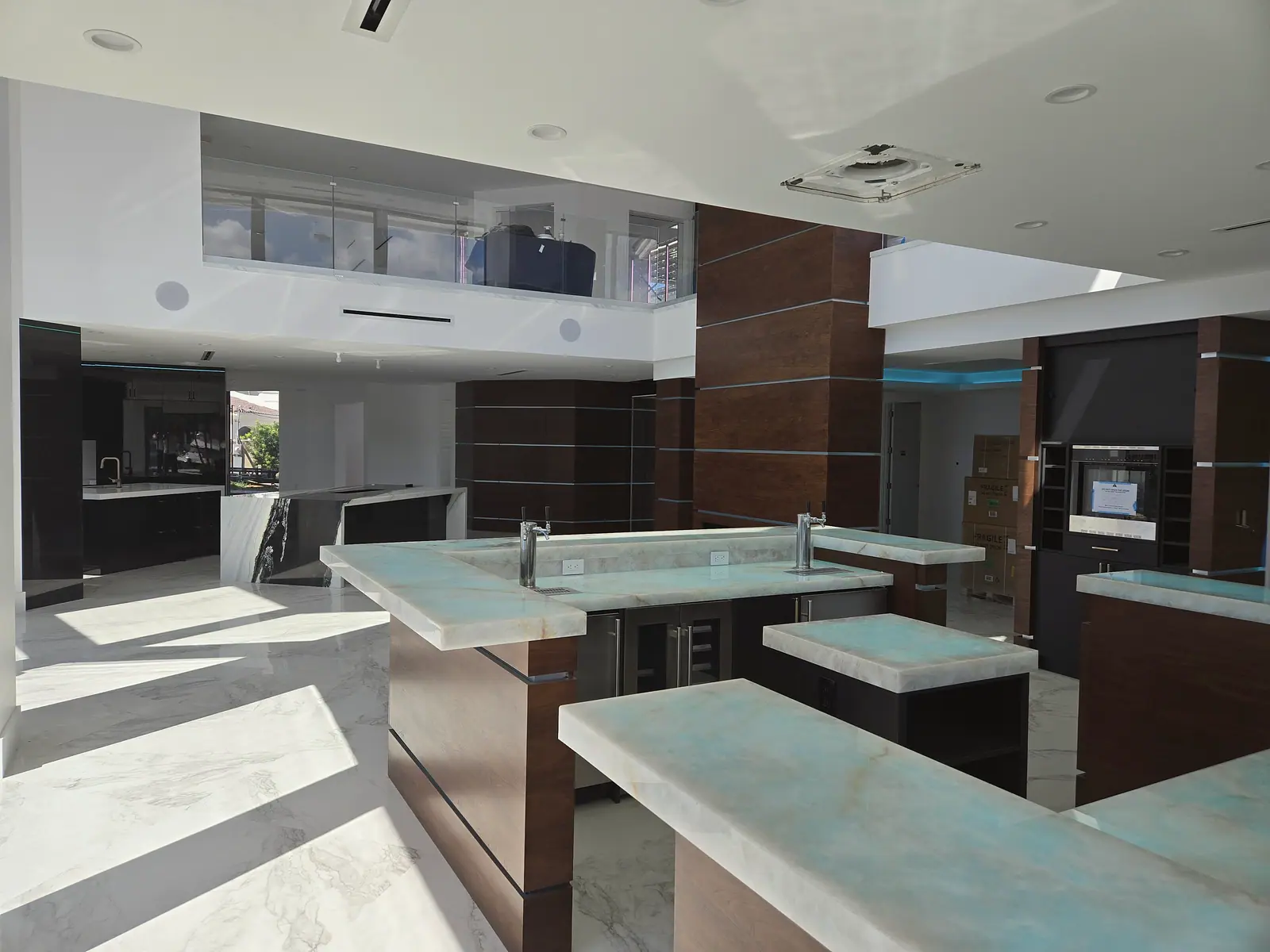Modern bar with blue veined quartzite counters and walnut cabinets under a glass railed mezzanine