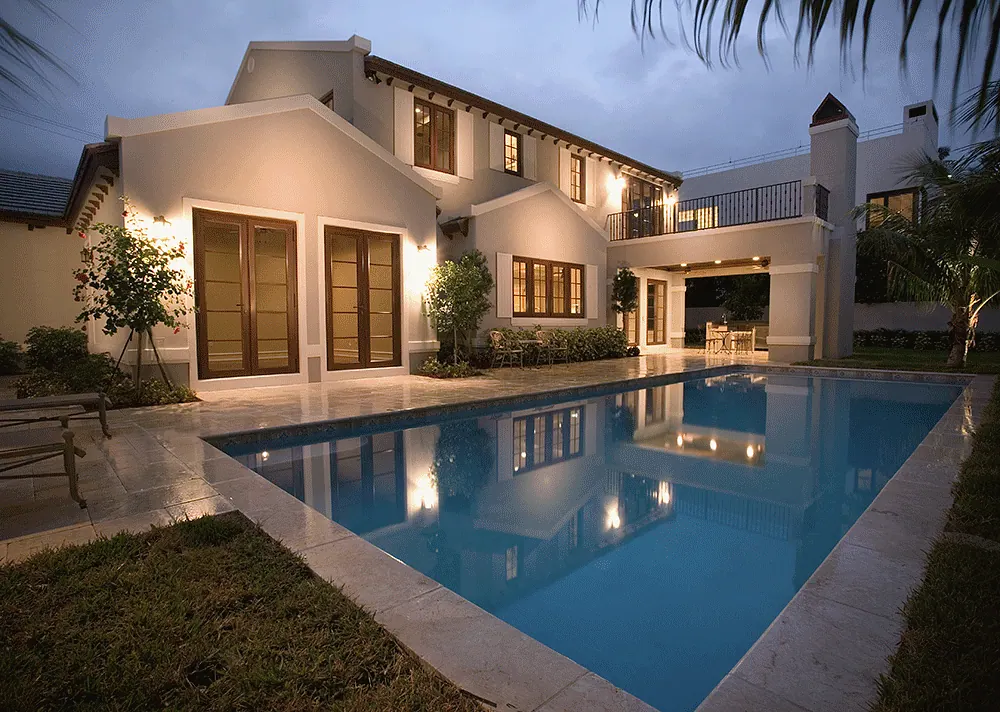 Lap pool beside a stucco house, lit at twilight