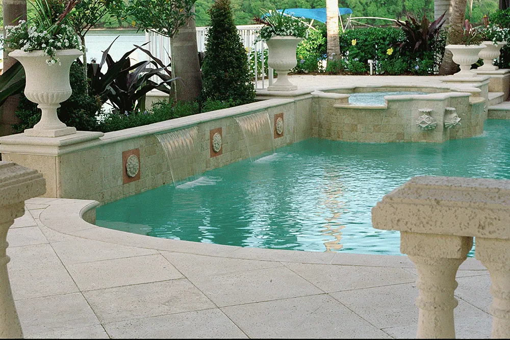 Pool with a stone fountain wall, planted urns and balustrades