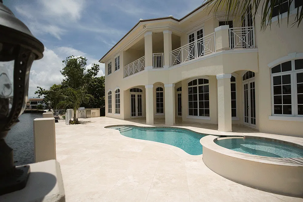 Freeform pool and spa on a stone deck behind a two-story house