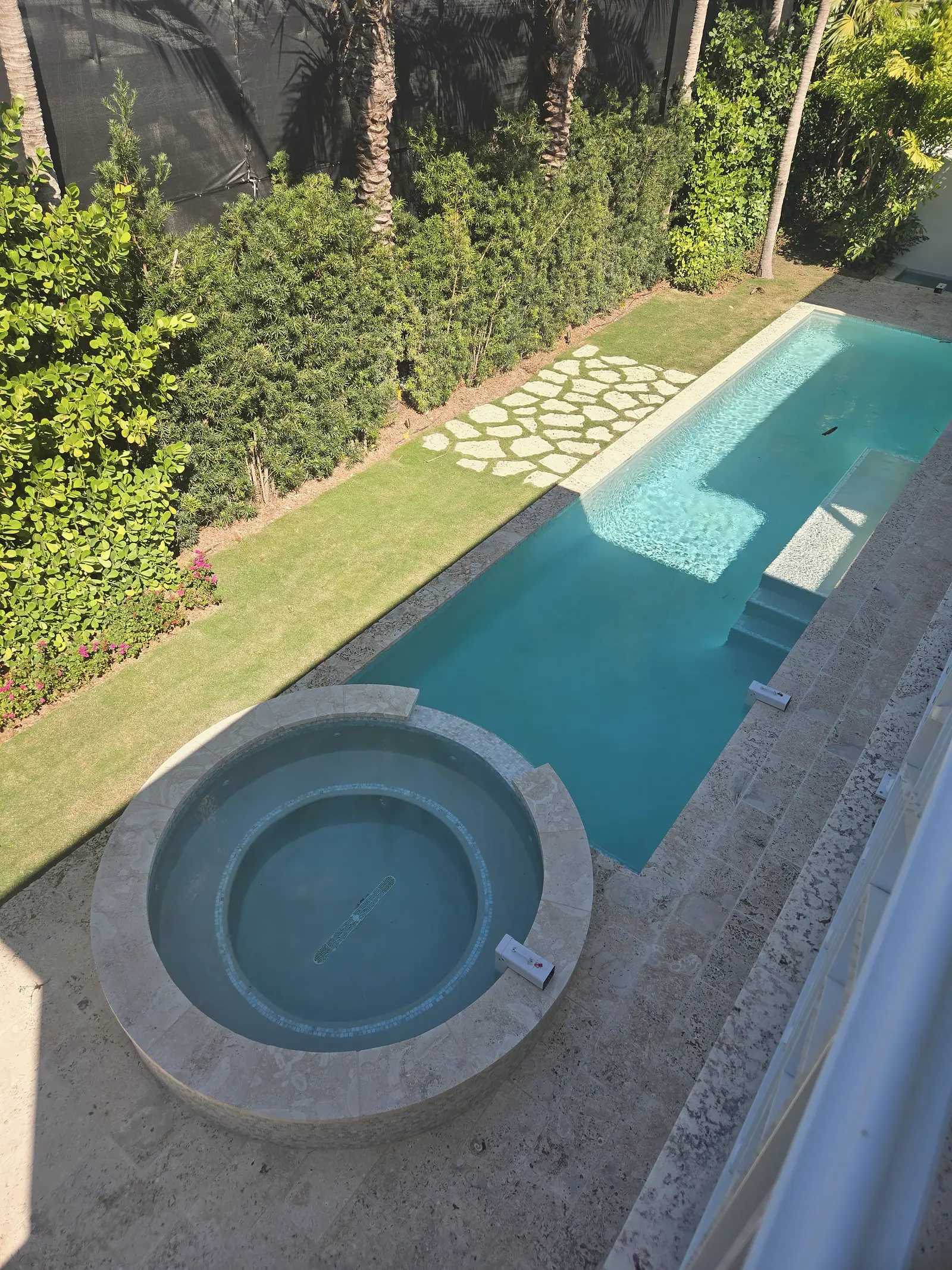 Overhead view of a long lap pool and round raised spa with stone coping, lawn and stepping stones beside a tall hedge
