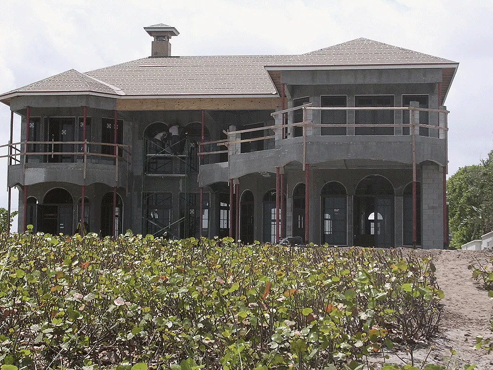 Two-story masonry house with arched openings behind sea grape, the roof on