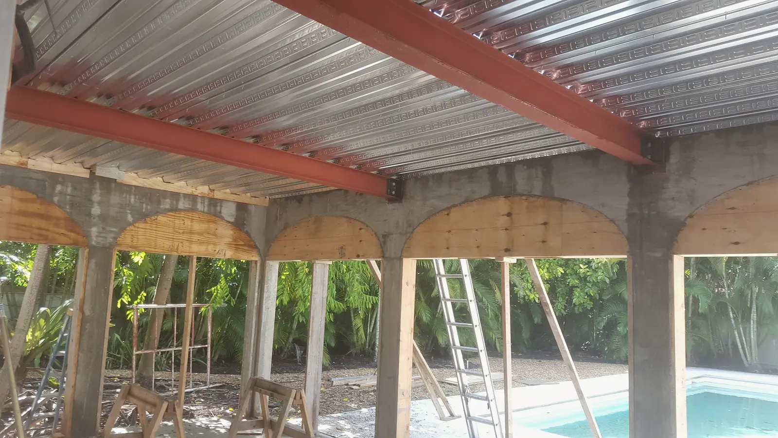Red steel beams and metal decking over a concrete arched loggia with plywood arch forms beside a pool