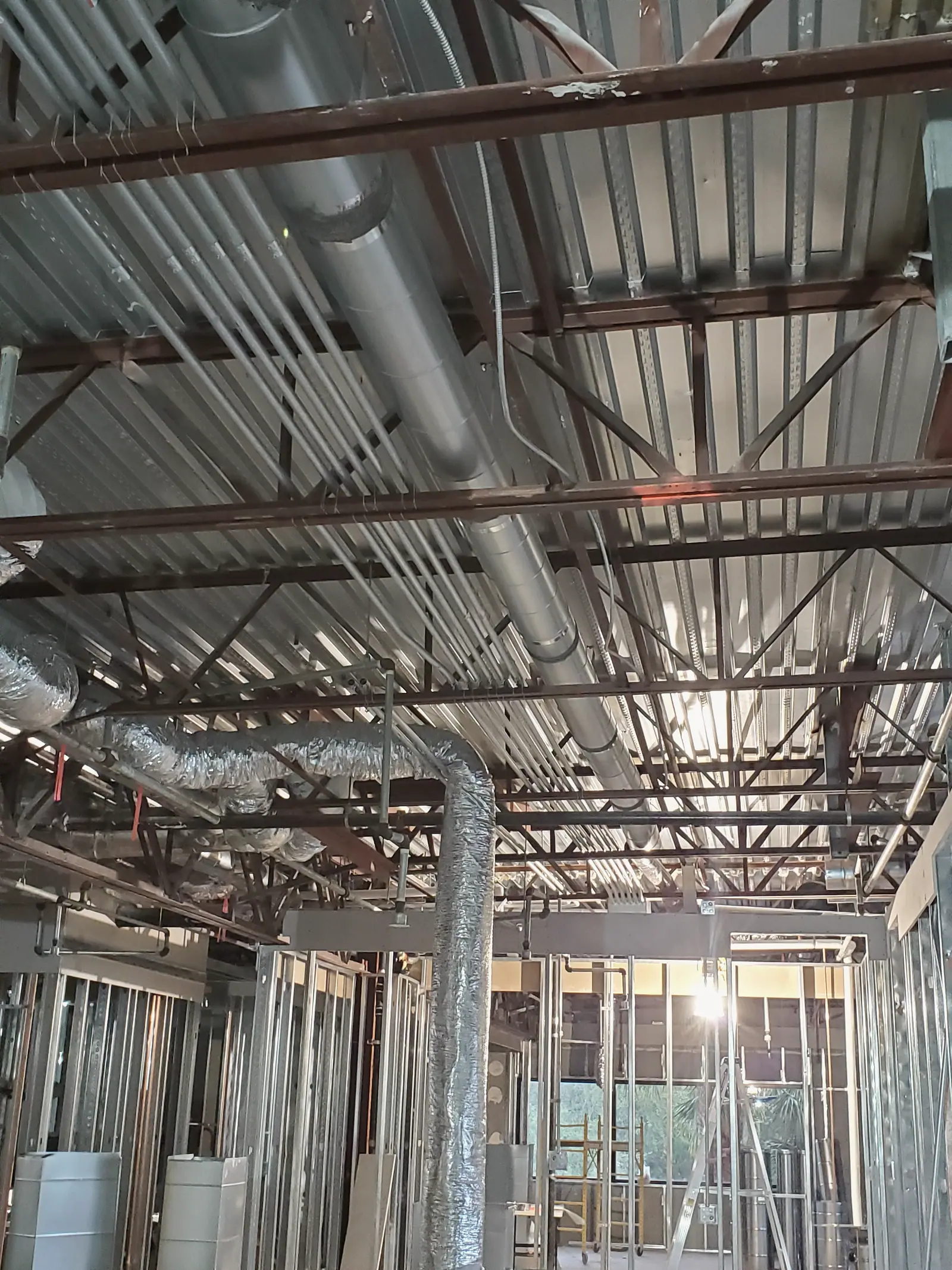 Exposed steel joists, spiral ducts and flexible ductwork above new metal stud walls