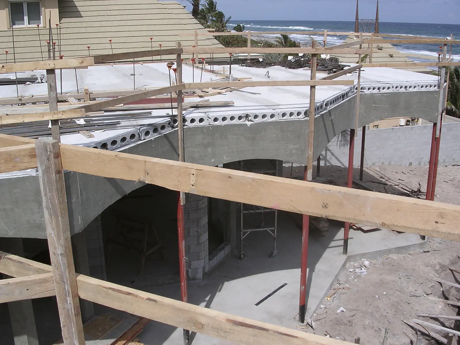 Hollow-core concrete planks resting on arched beams with red shoring posts and the ocean in the background